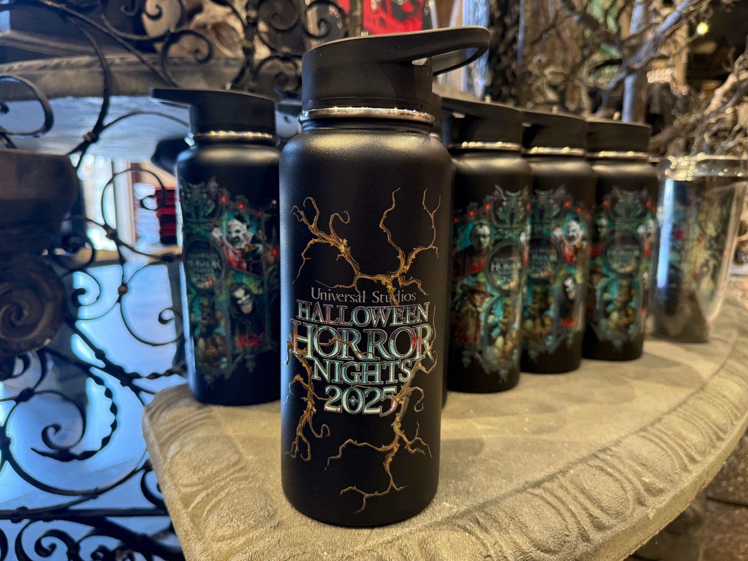 A black water bottle displays "Halloween Horror Nights 2023" surrounded by spooky artwork, with more bottles behind it.