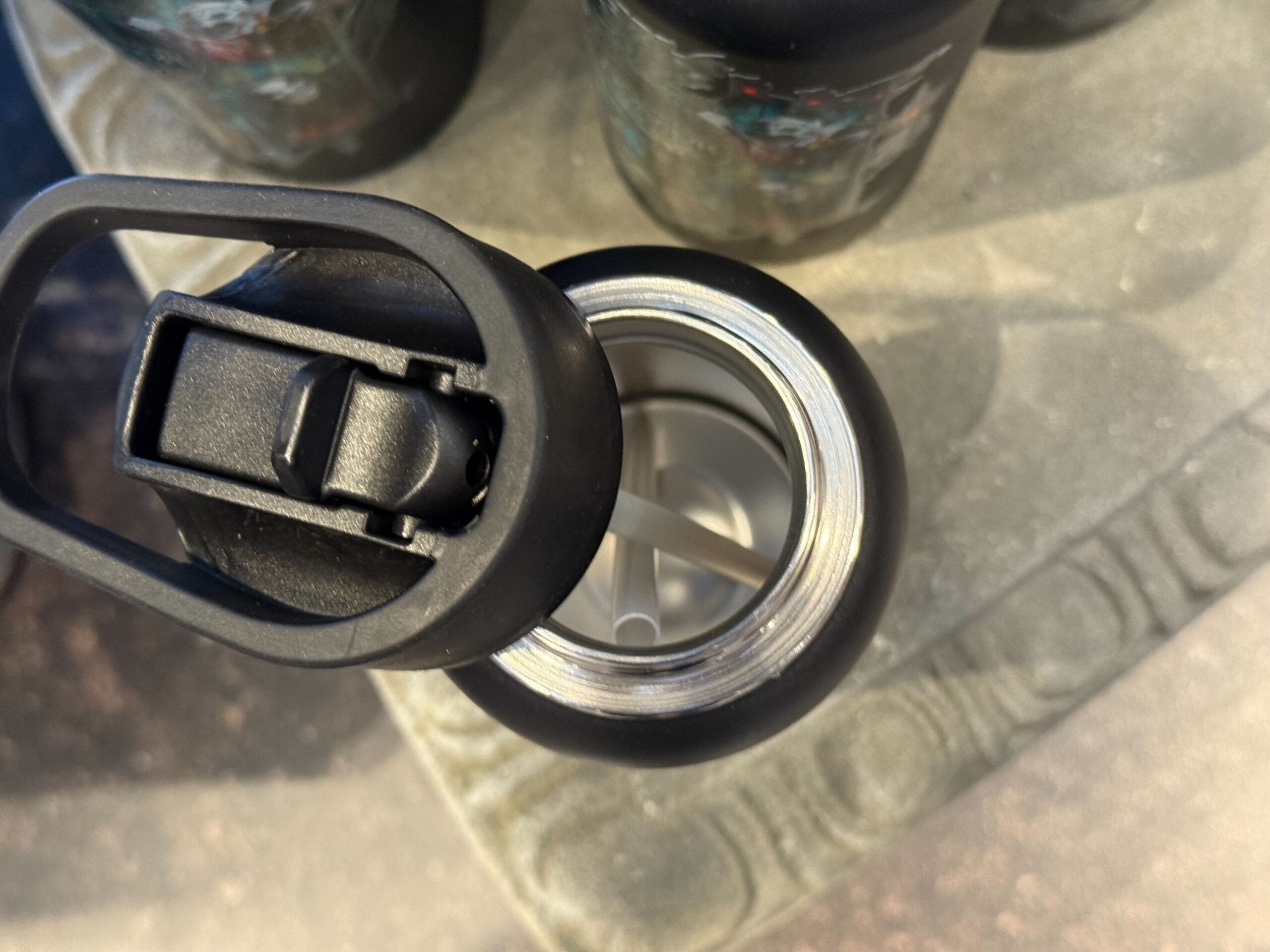 Open black water bottle with a straw, viewed from above, on a textured gray surface.