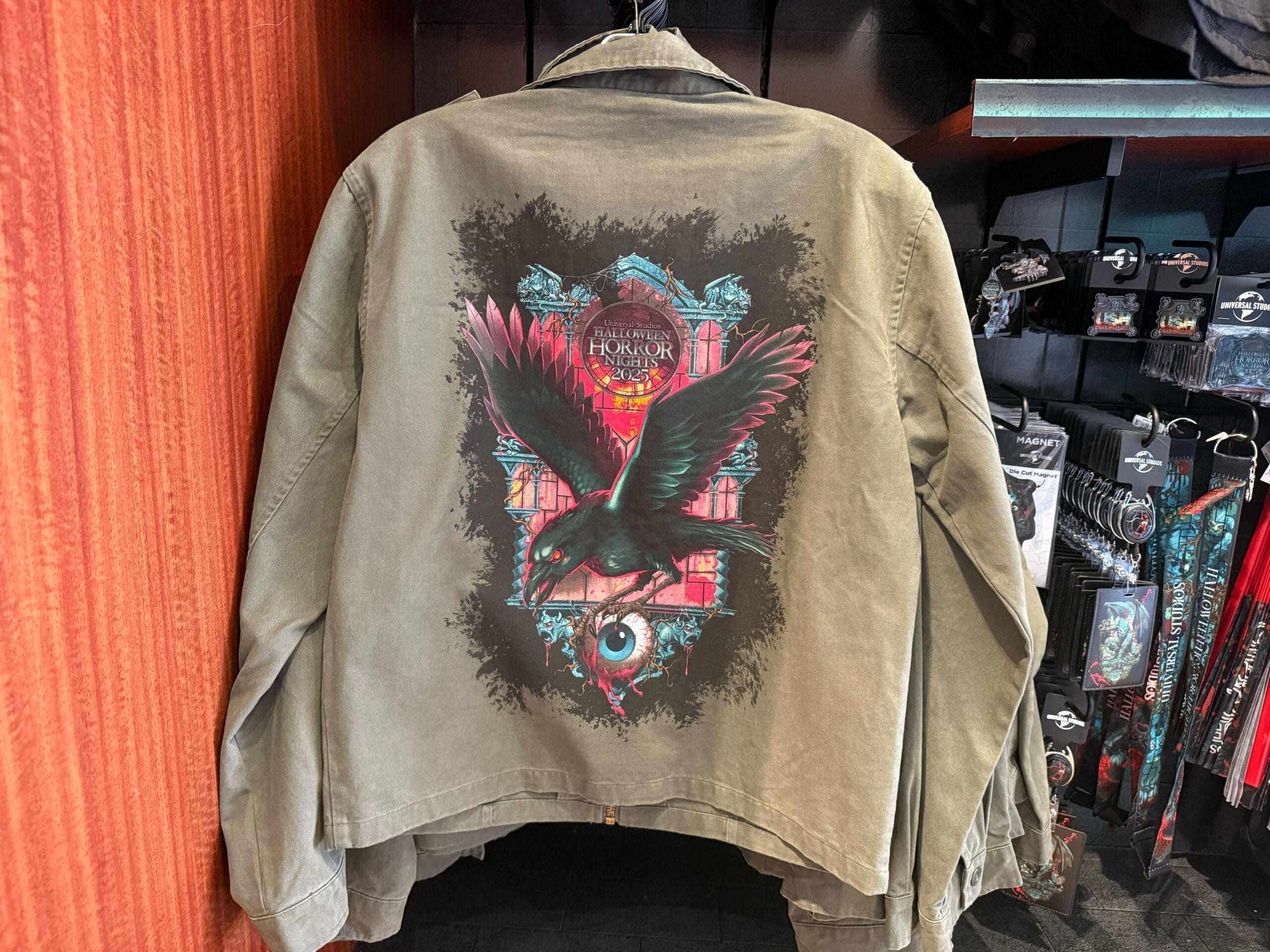 Olive jacket featuring a raven, eye, and Gothic architecture—perfect Halloween Horror Nights Merchandise from Universal Studios Hollywood.