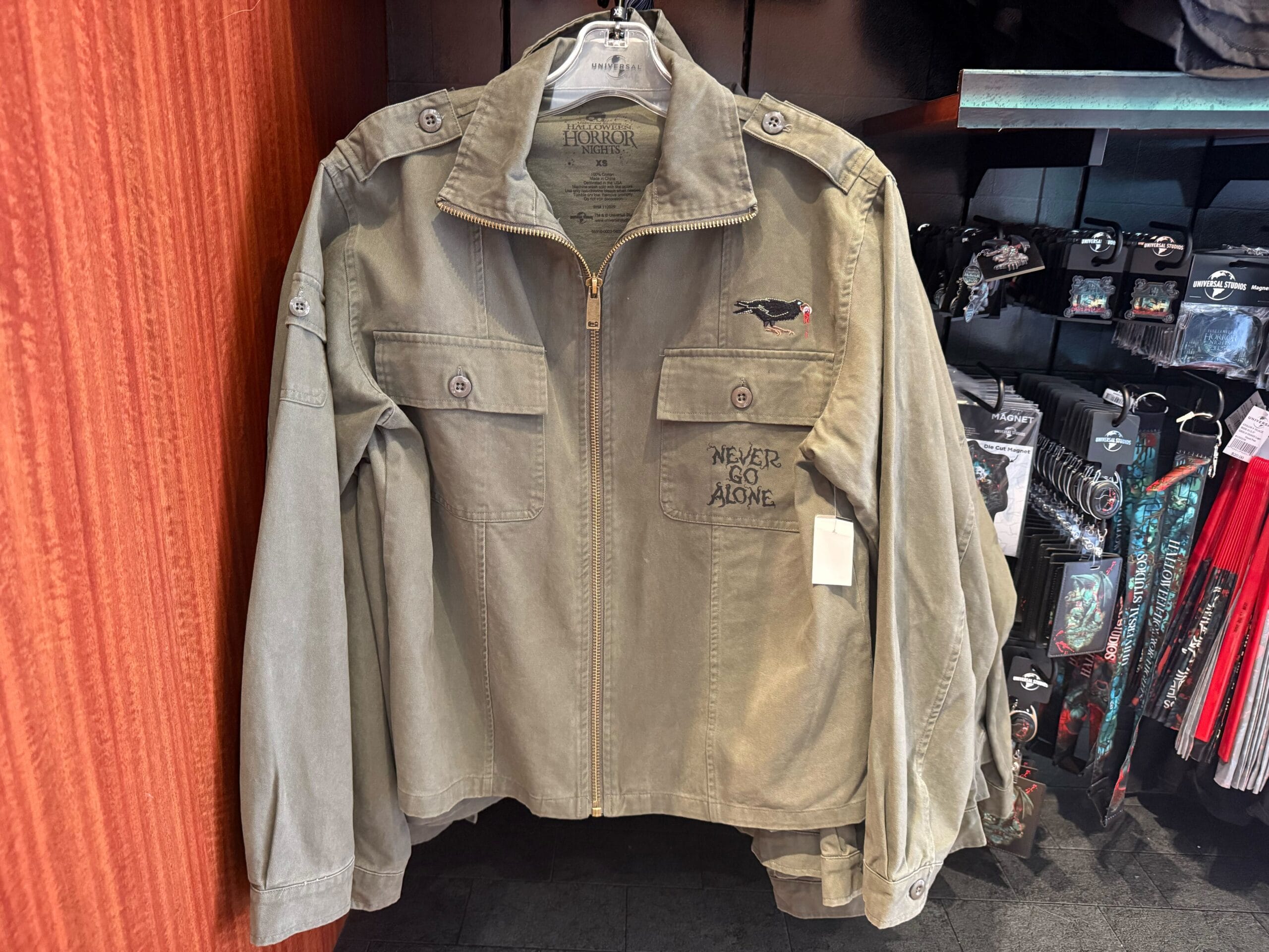 Olive green jacket with "Never Go Alone" and an embroidered raven—exclusive HHN Merch 2025 at Universal Studios Hollywood.