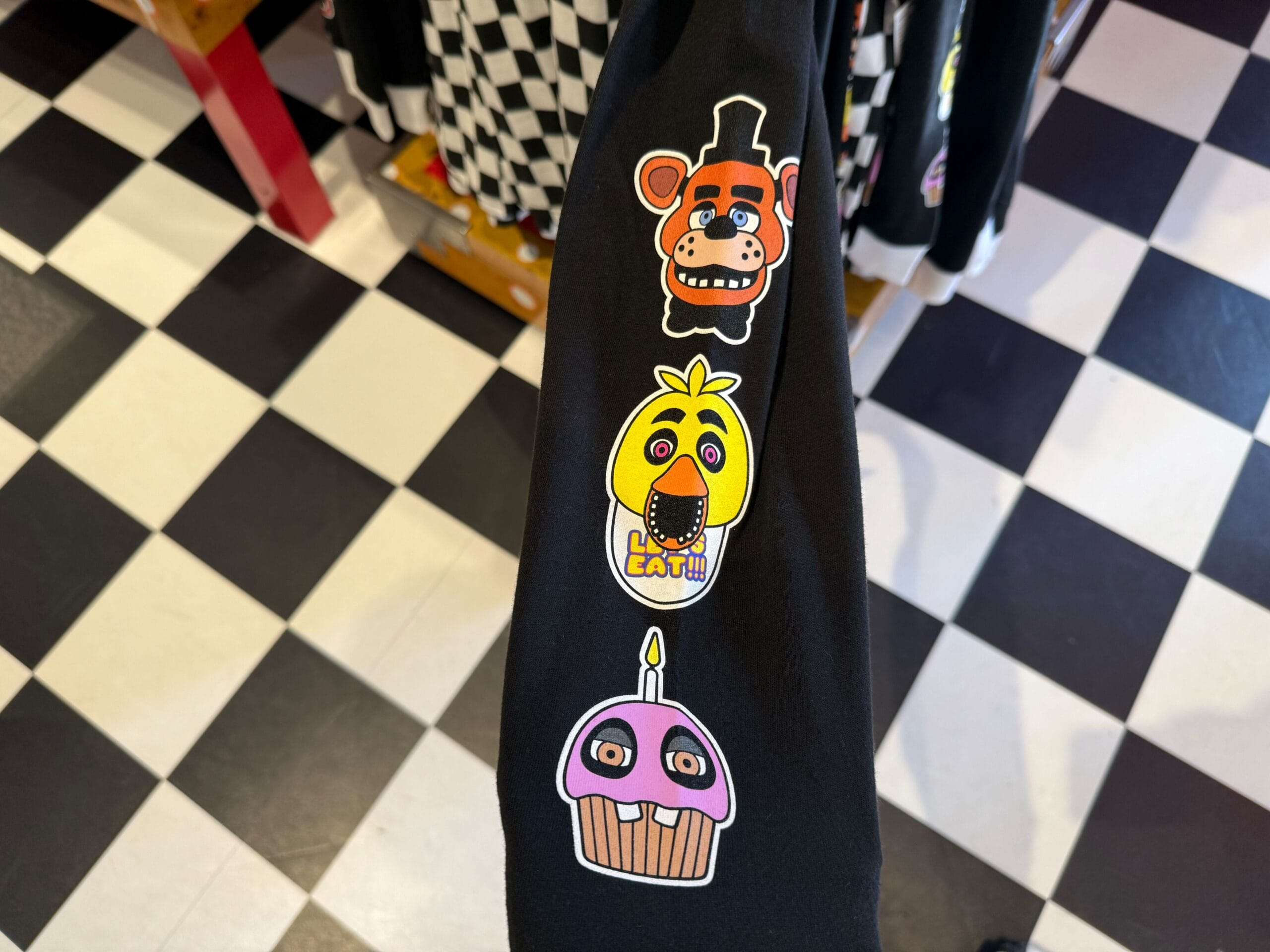 Black sleeve with colorful cartoon bear, chicken, and cupcake faces—perfect for HHN Merch 2025 at Universal Studios Hollywood.