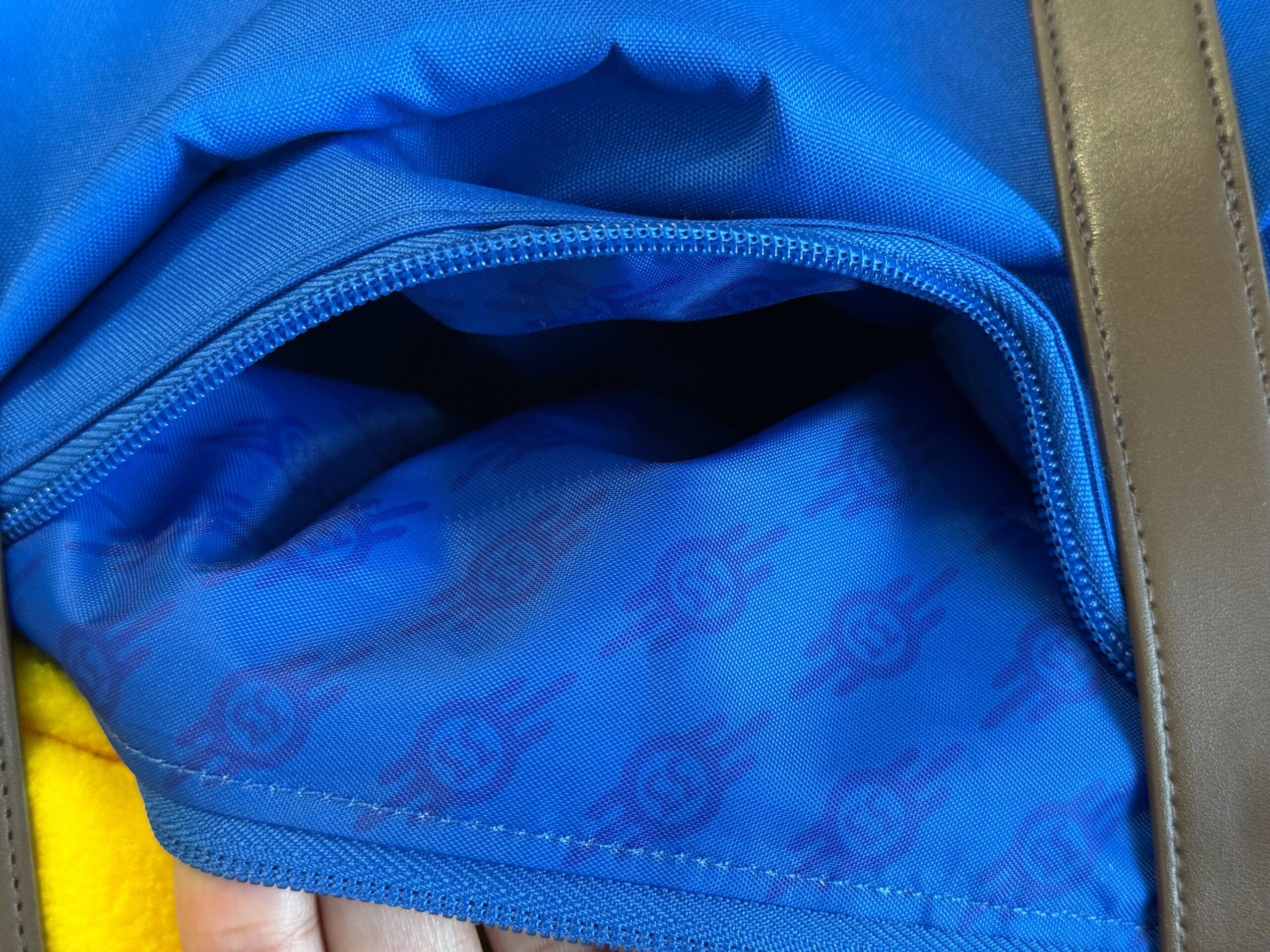 A close-up of a blue zippered bag pocket with patterned lining and brown straps, part of HHN Merch 2025.