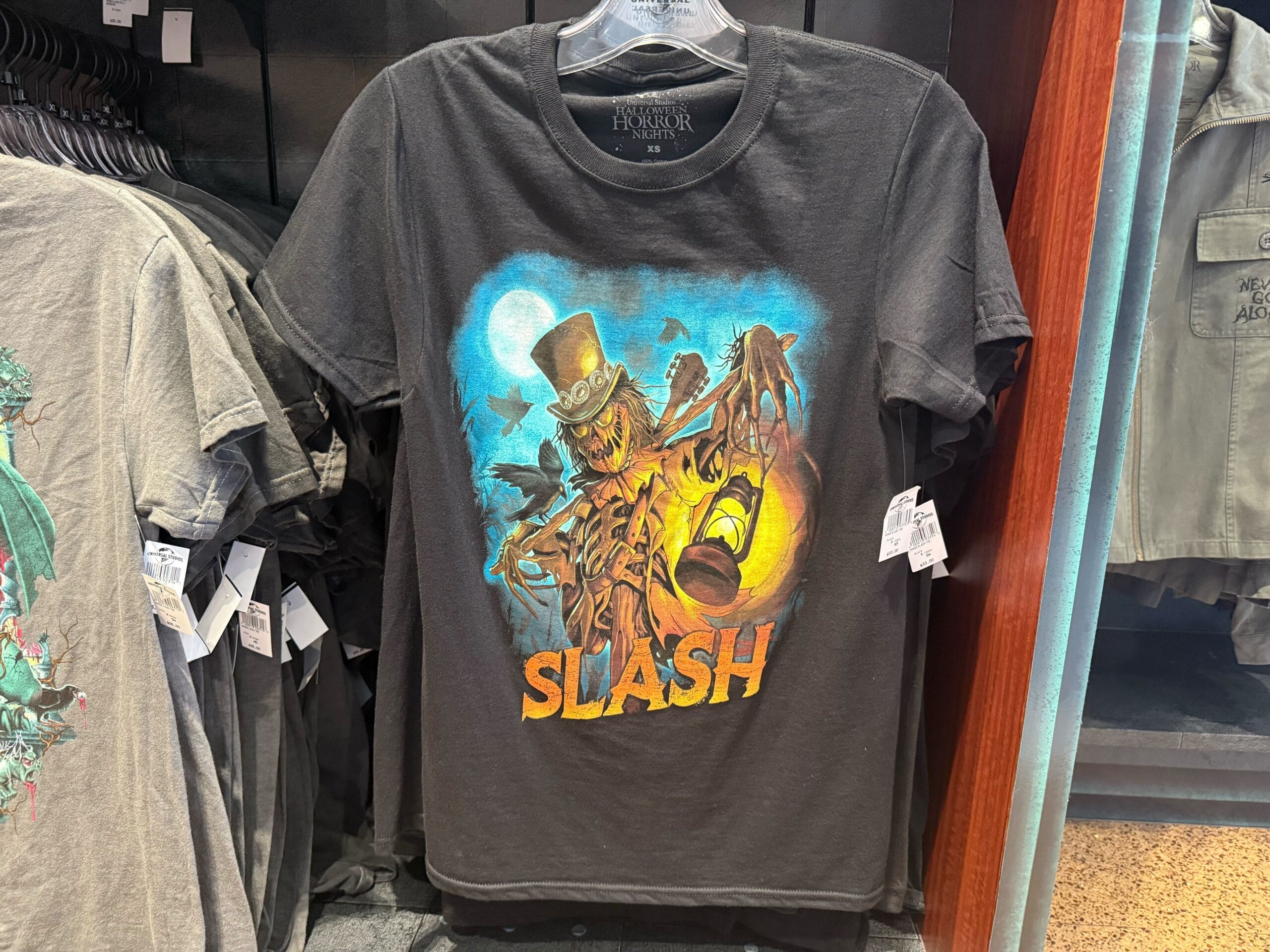 Black t-shirt with a scarecrow in a top hat, bats, "SLASH" text—perfect Halloween Horror Nights Merchandise.
