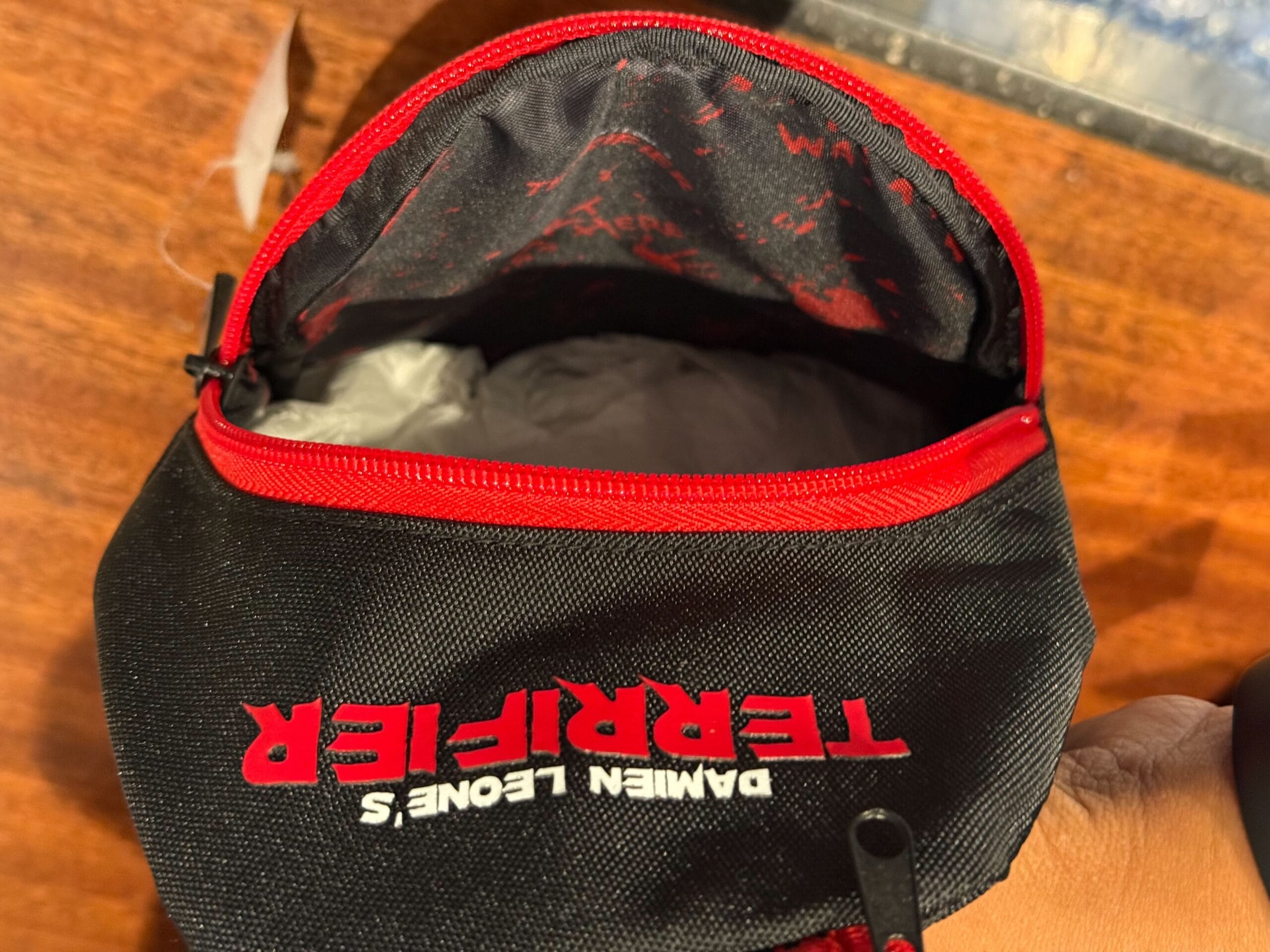 A black and red zippered pouch with "DAMIEN LEONE'S TERRIFIER," perfect for Halloween Horror Nights Merchandise fans.