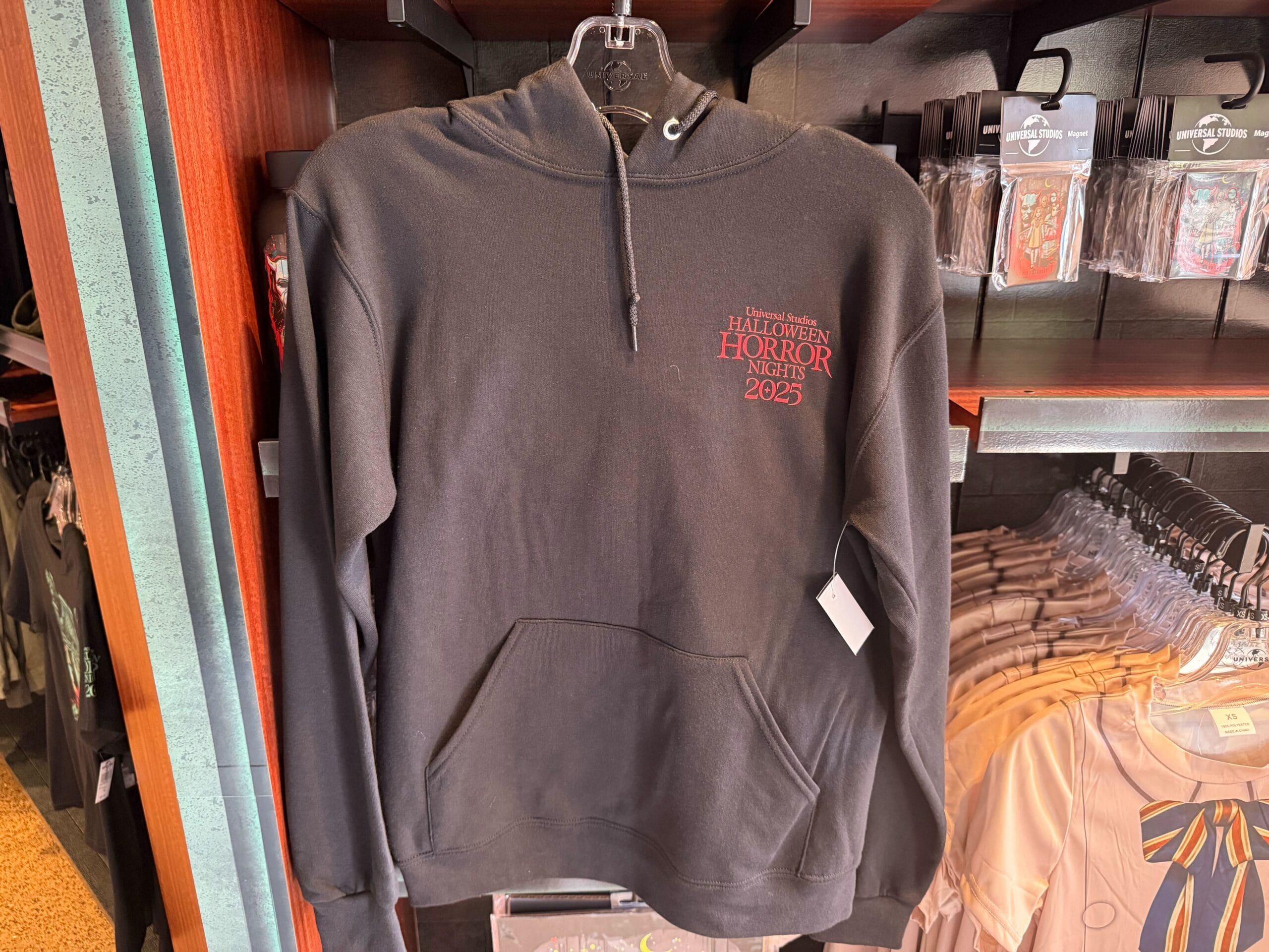 Black hoodie with "Halloween Horror Nights 2023" in red, classic Universal Studios Hollywood merchandise on display rack.