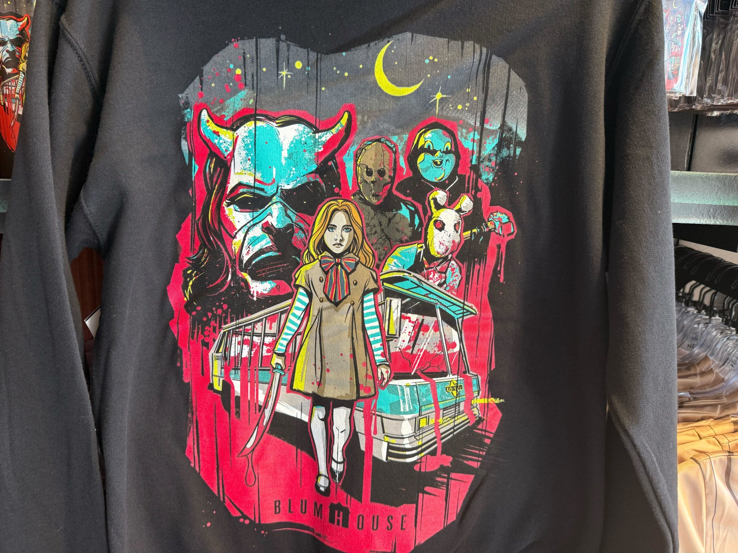 A shirt features creepy masked figures and a girl before a blood-spattered house—perfect Halloween Horror Nights Merchandise.