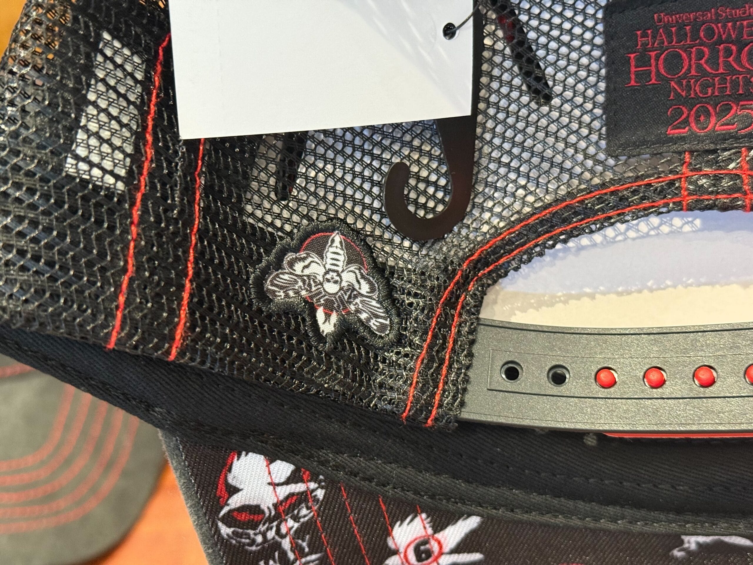 Close-up of a black mesh cap with HHN Merch and creepy clown pin, labeled "Halloween Horror Nights 2023.