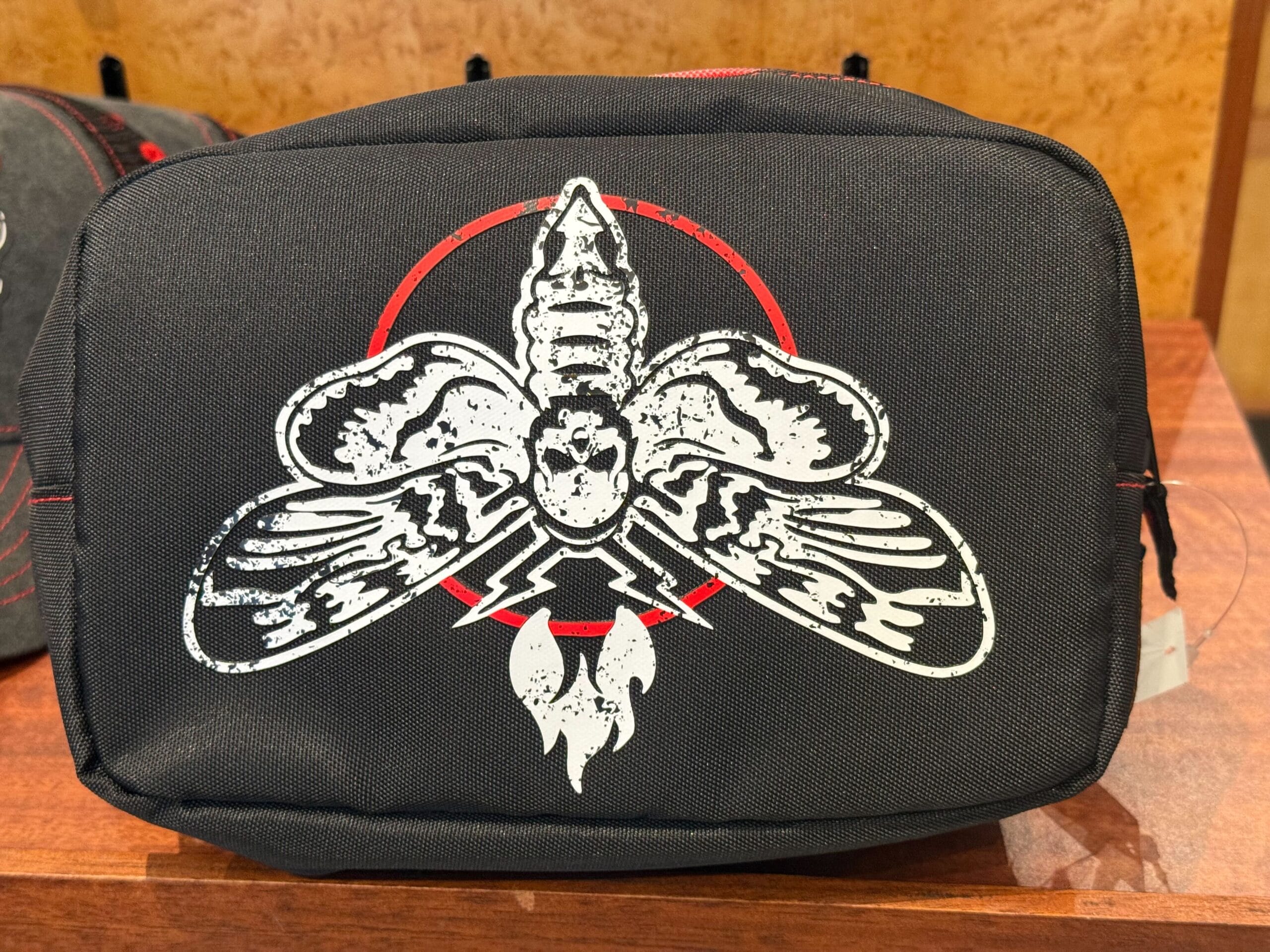 A black pouch with a white stylized insect and red circle, perfect for Halloween Horror Nights Merchandise collectors.