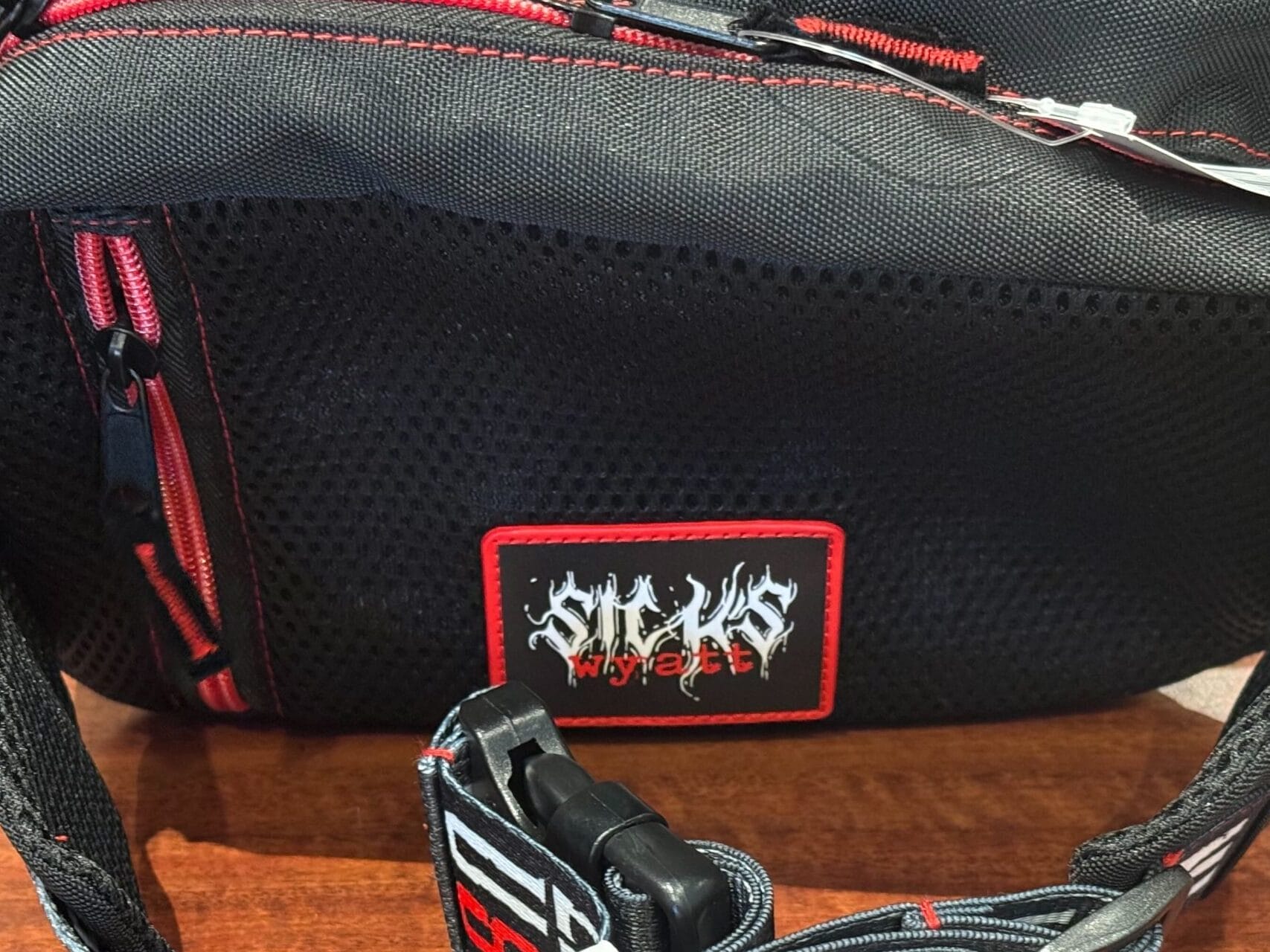 A black waist bag with red zippers and logo, inspired by Halloween Horror Nights Merchandise, on a wooden surface.