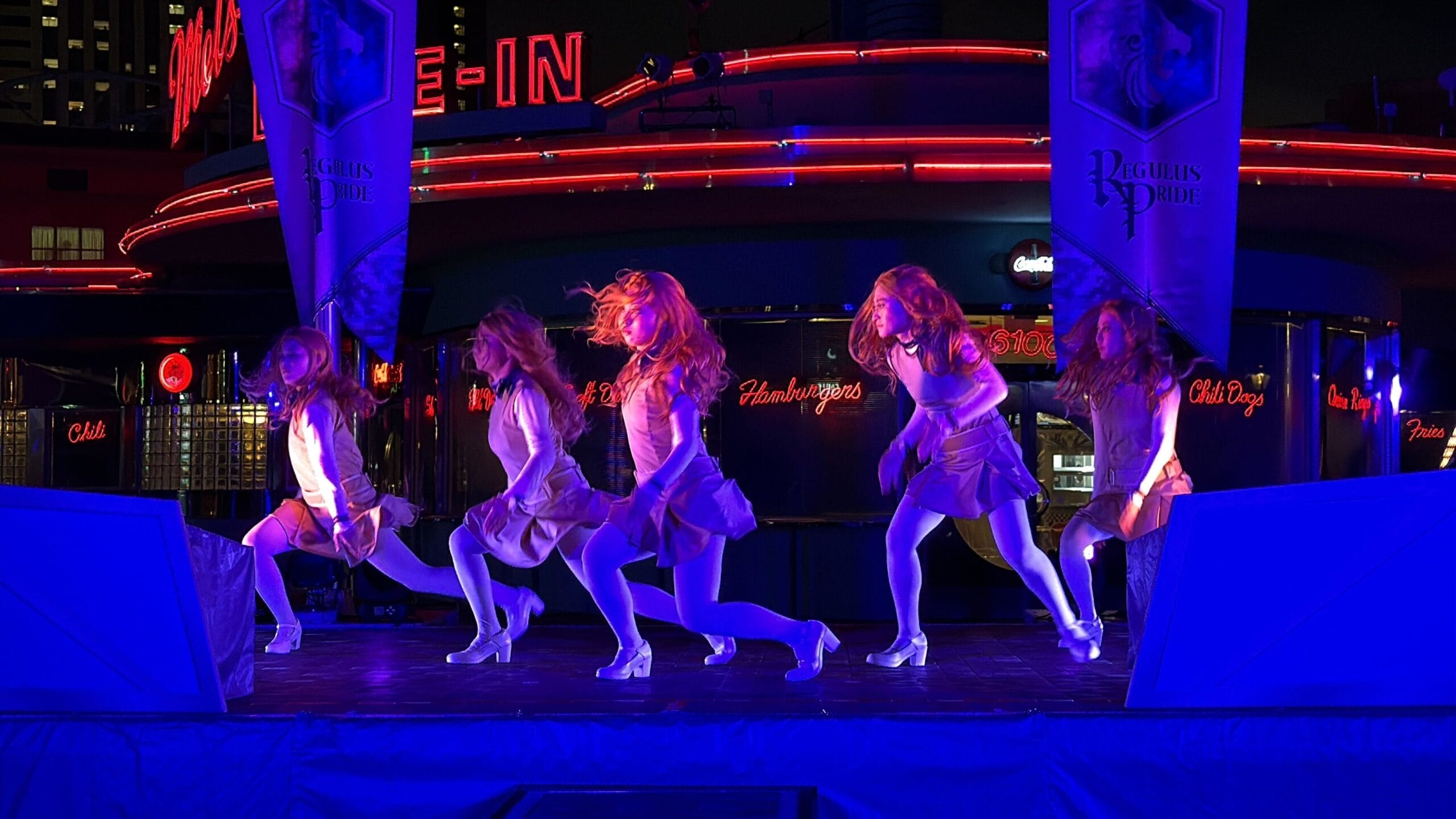 Five dancers in matching white outfits perform as the M3GAN Horde on a neon-lit Universal Studios Japan stage.