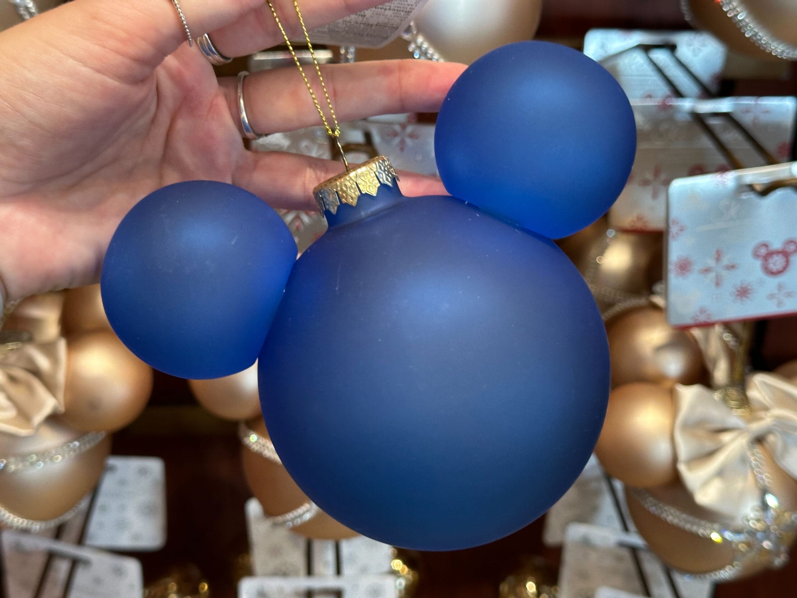 A hand holds a blue Mickey Mouse ornament among other festive holiday ornaments.