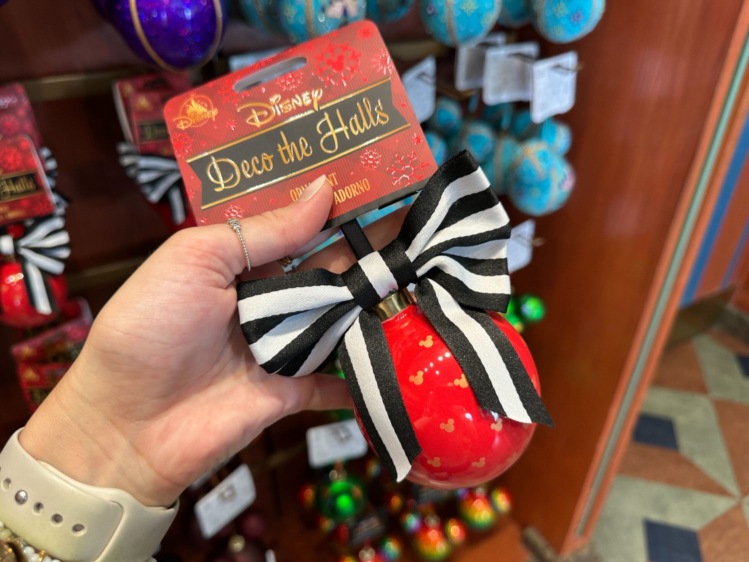 A hand holds a red Mickey Mouse ornament with a black and white striped bow in a store display.