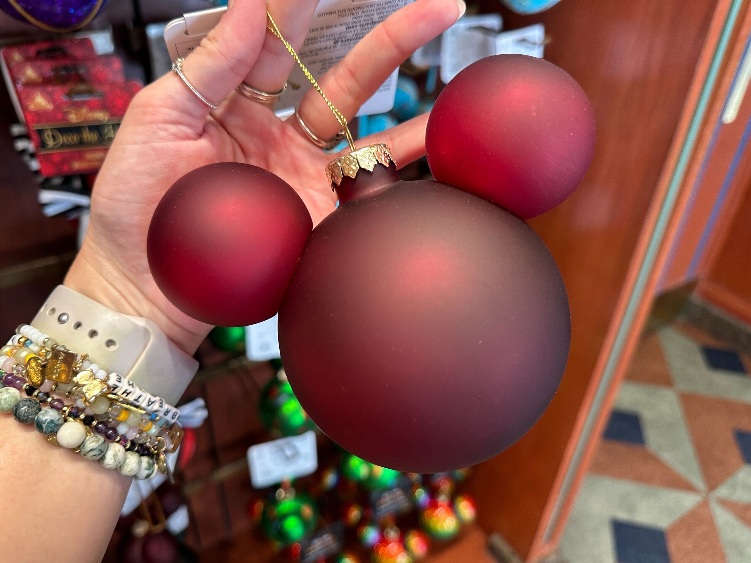 A hand holds a red Mickey Mouse-shaped holiday ornament in a Disney World store.
