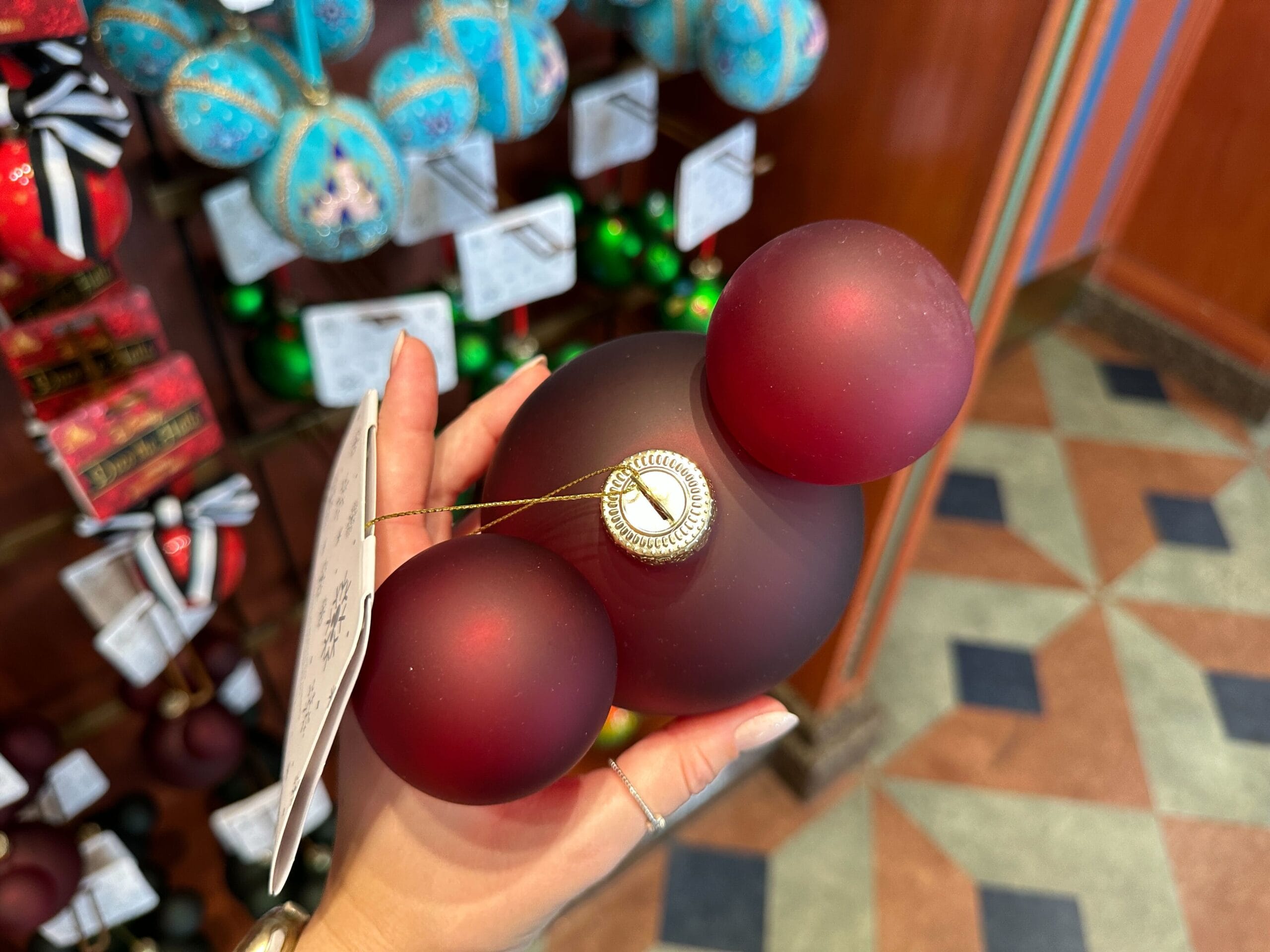 A hand holds a red Mickey Mouse-shaped holiday ornament in a store filled with Disney World Christmas ornaments.