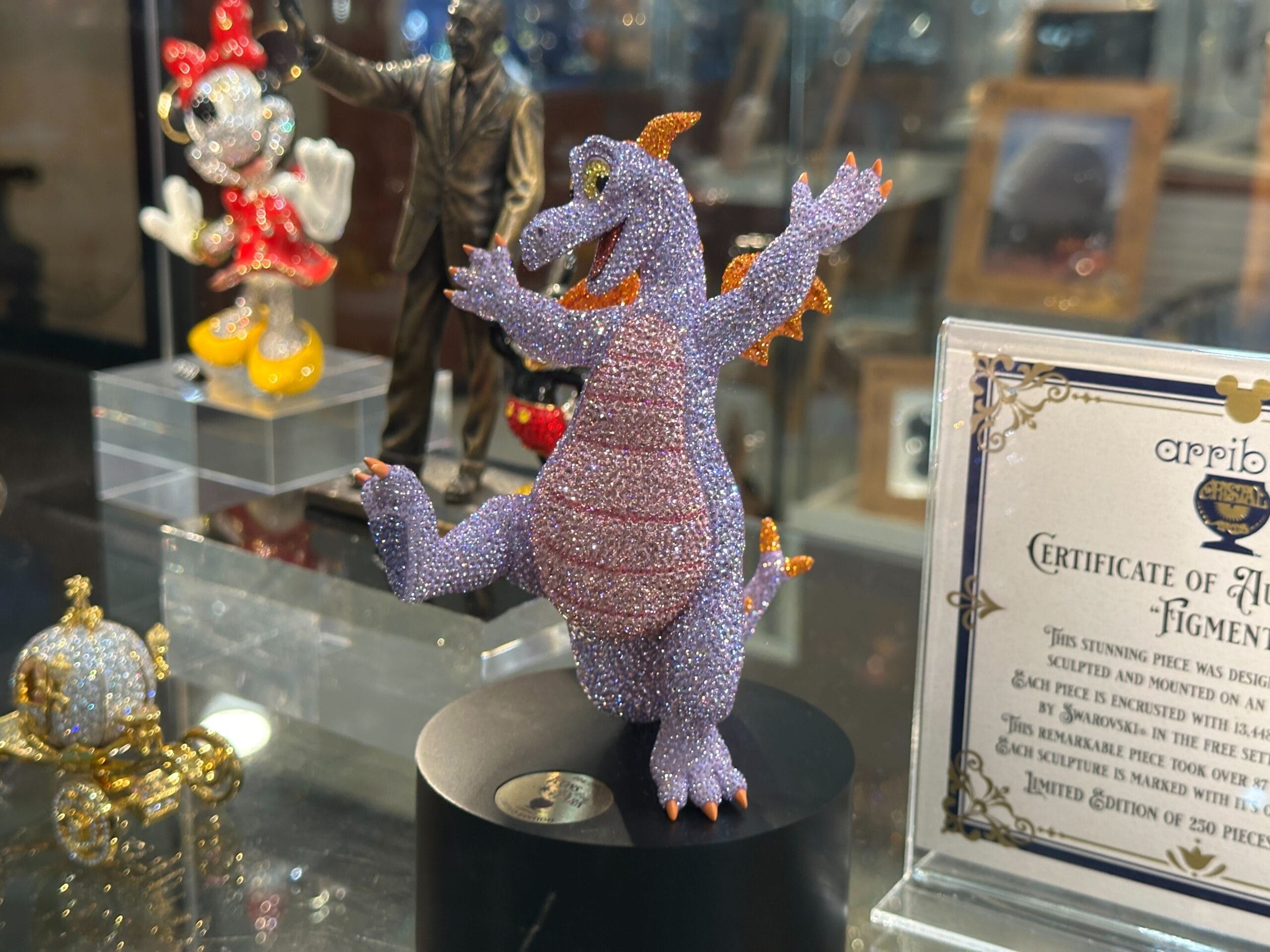 A sparkling, jewel-encrusted dragon figurine on display, with other decorative items and a certificate in the background.