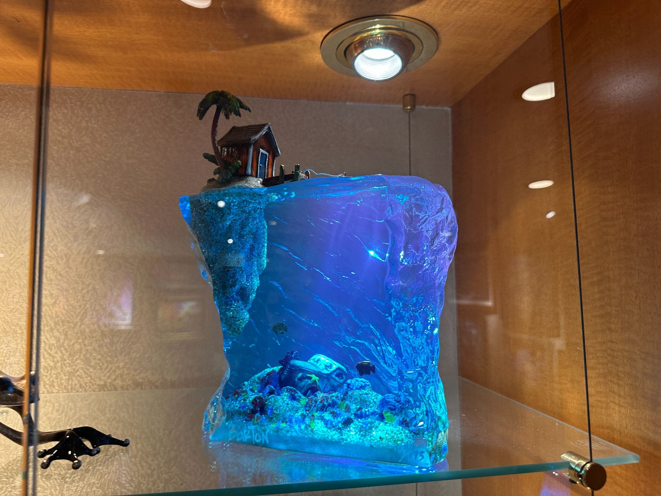 A resin art piece shows an island hut above water and a sunken treasure chest below, displayed in a glass cabinet.