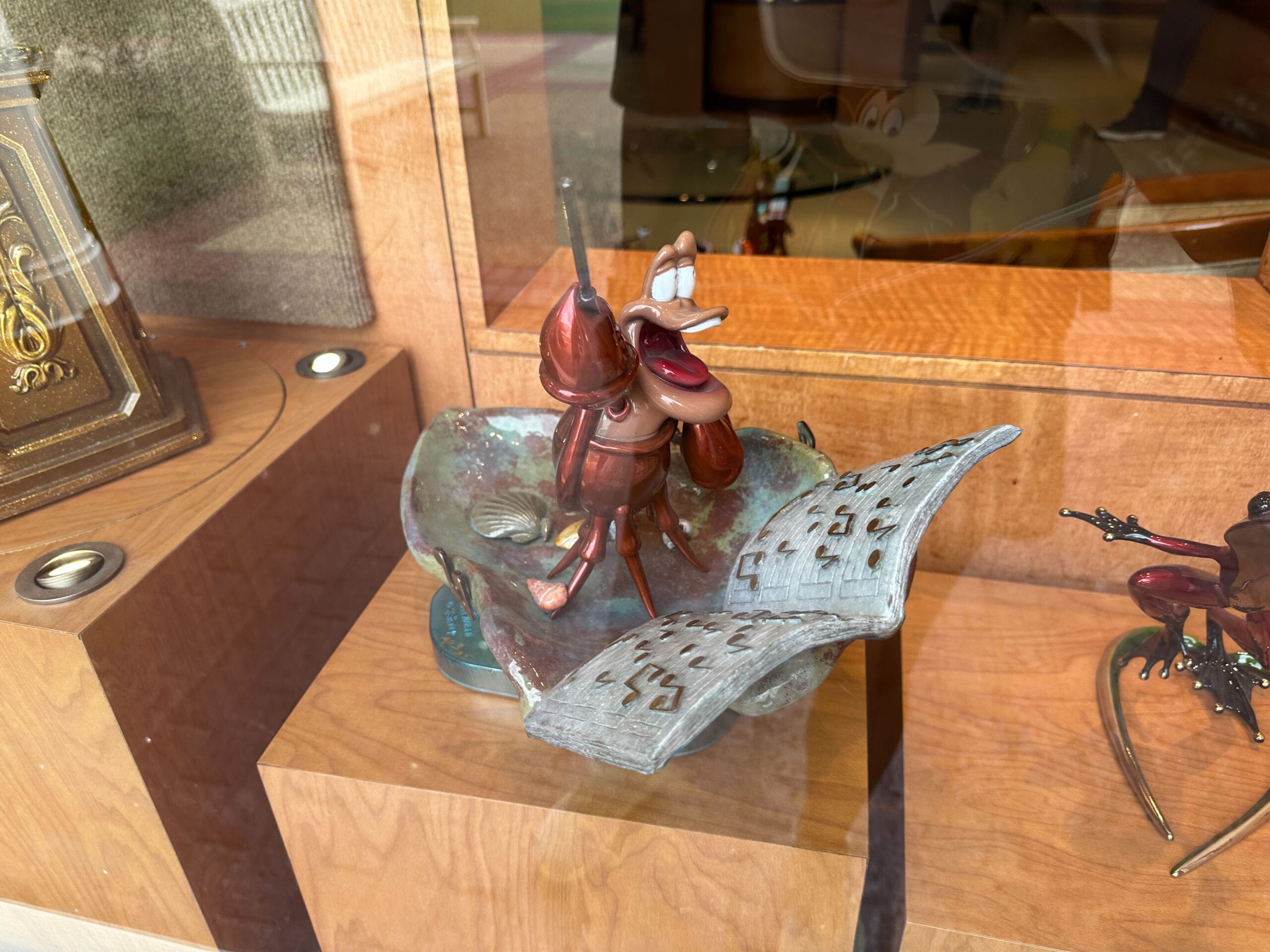 A cartoonish bronze ant sculpture reading a large book, displayed inside a wooden glass case.