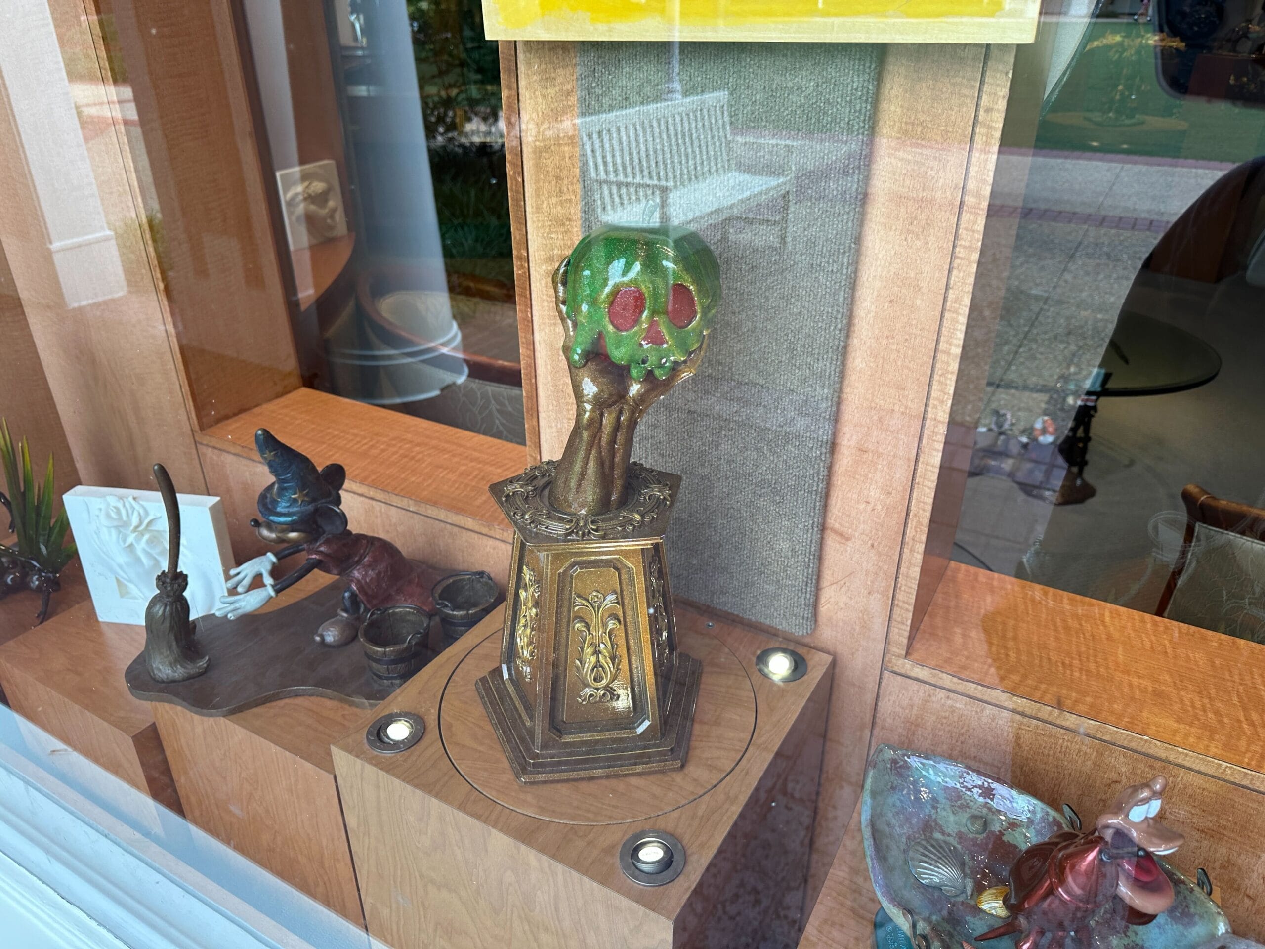 A decorative green apple sculpture with red accents on a gold pedestal displayed in a wooden window case with other art objects.