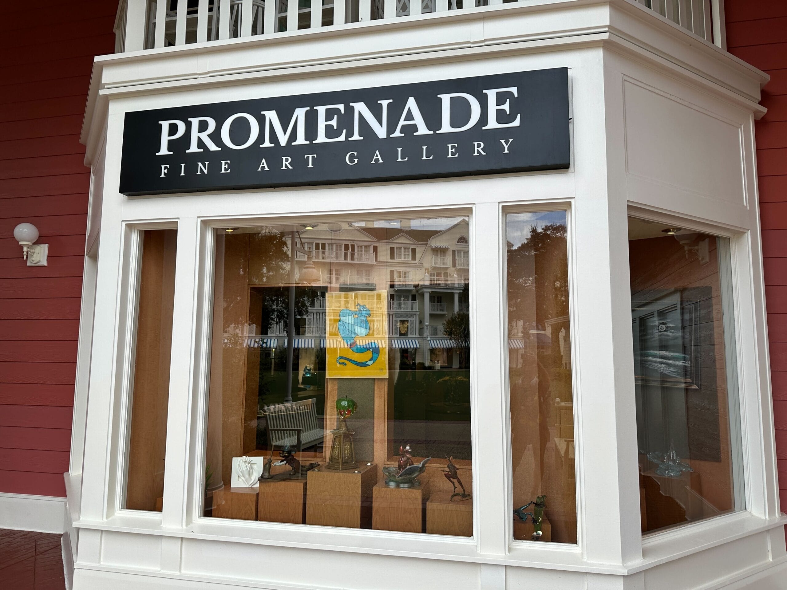 Storefront window of "Promenade Fine Art Gallery" with art pieces displayed inside and reflections of buildings outside.