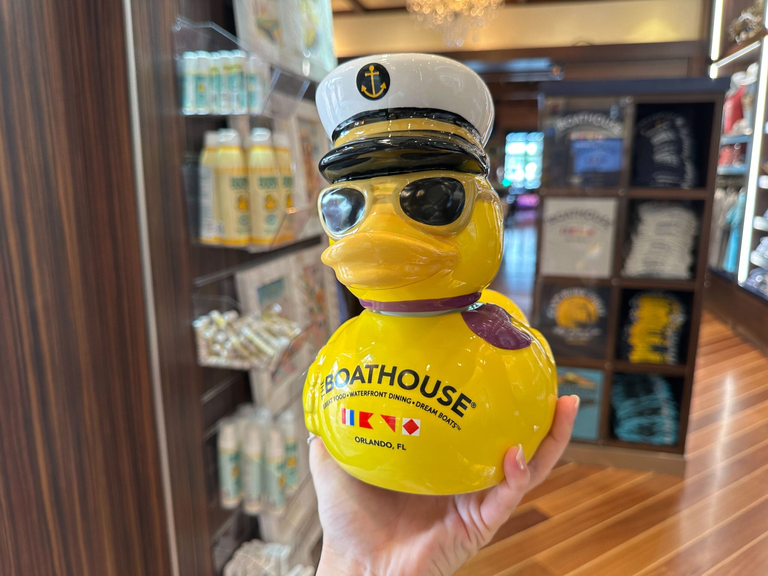 A hand holds a yellow rubber duck wearing a captain's hat and sunglasses, labeled "The Boathouse, Orlando, FL.