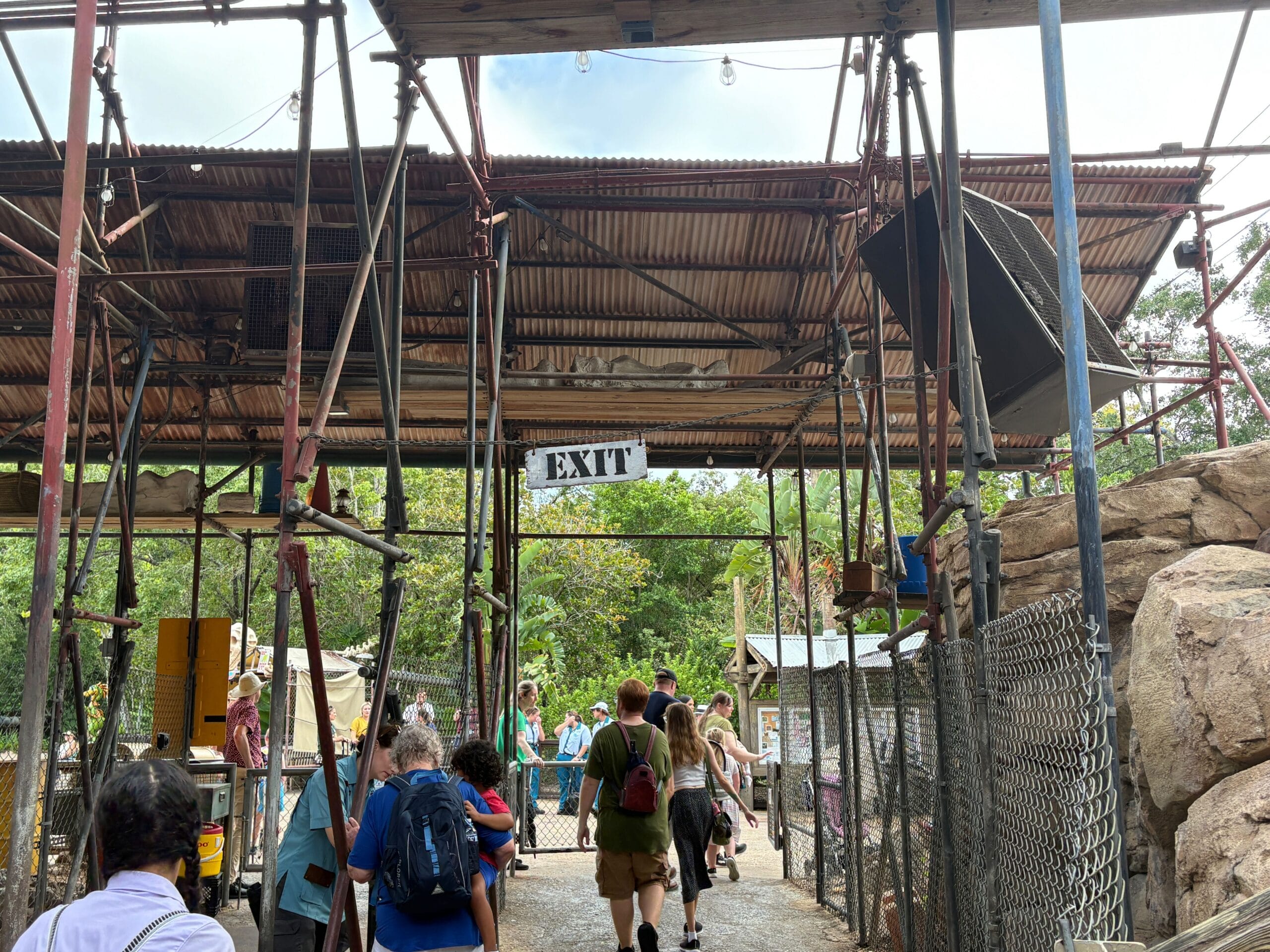 People walk under a metal awning near the closed Boneyard at Disney's Animal Kingdom on a sunny day.
