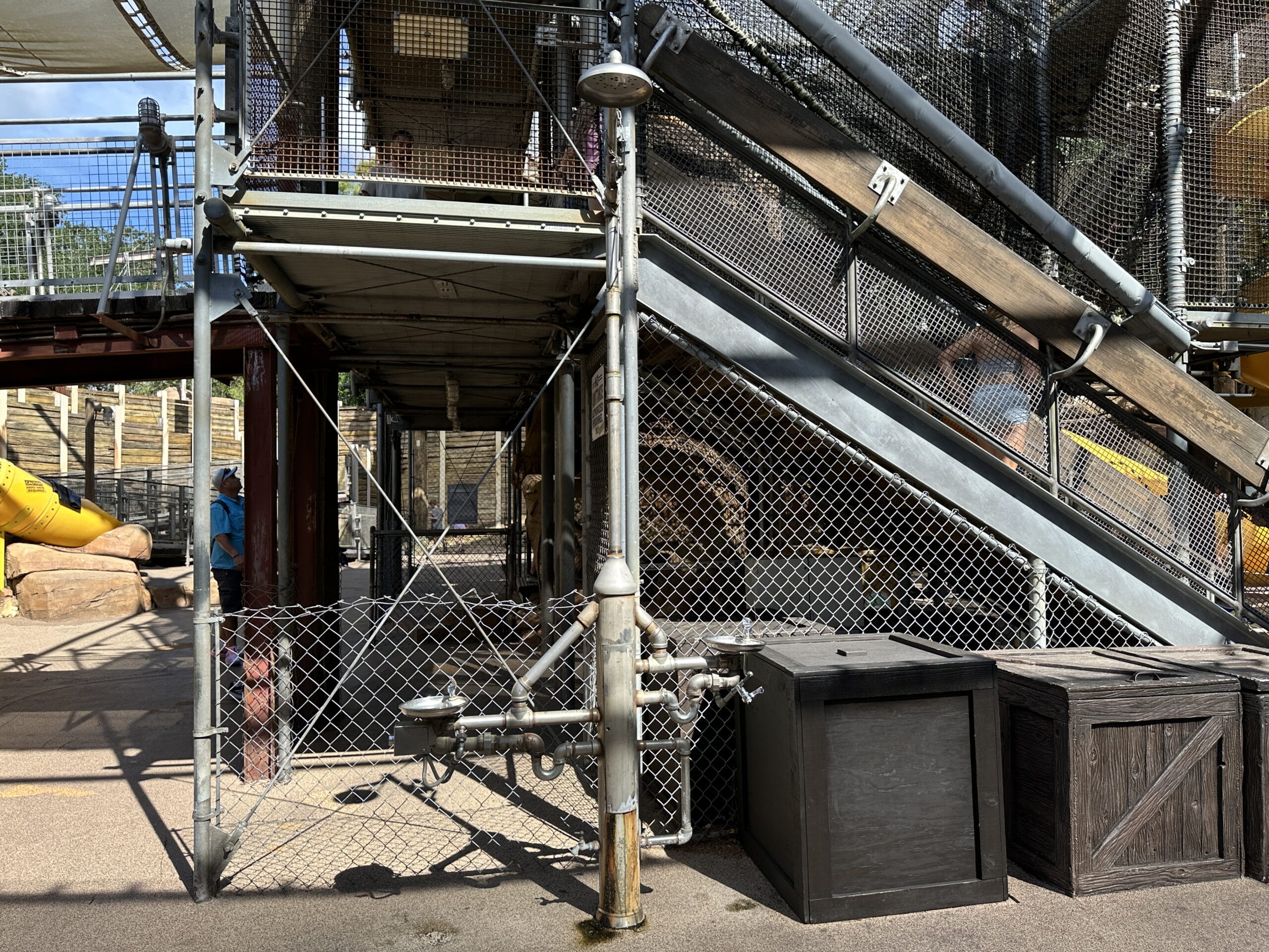 Outdoor staircase with metal railings, pipes, crates, and wire fencing near a playground structure.