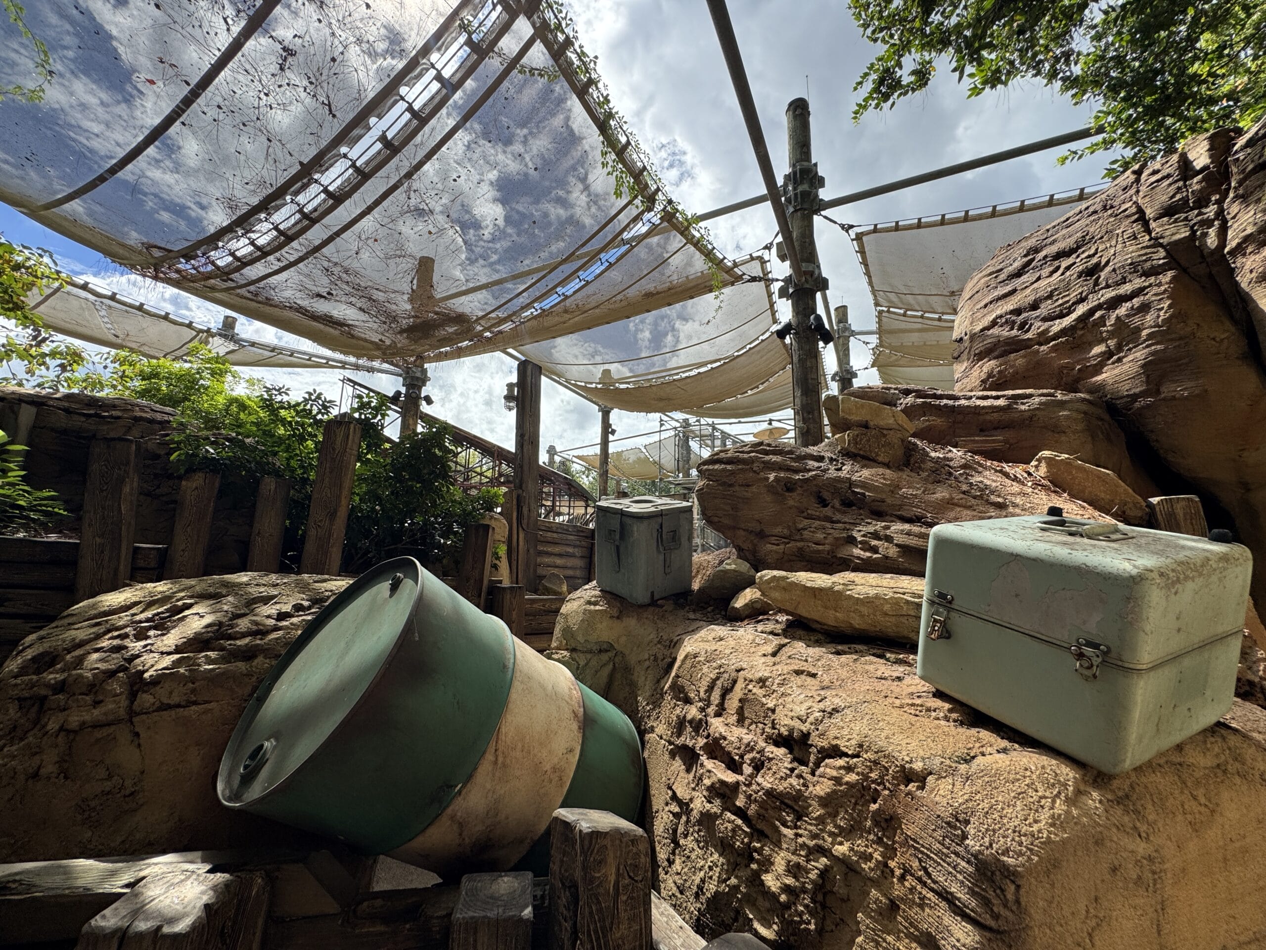 Large rocks and barrels under shade cloths at The Boneyard, sunlight filtering through at Disney's Animal Kingdom.
