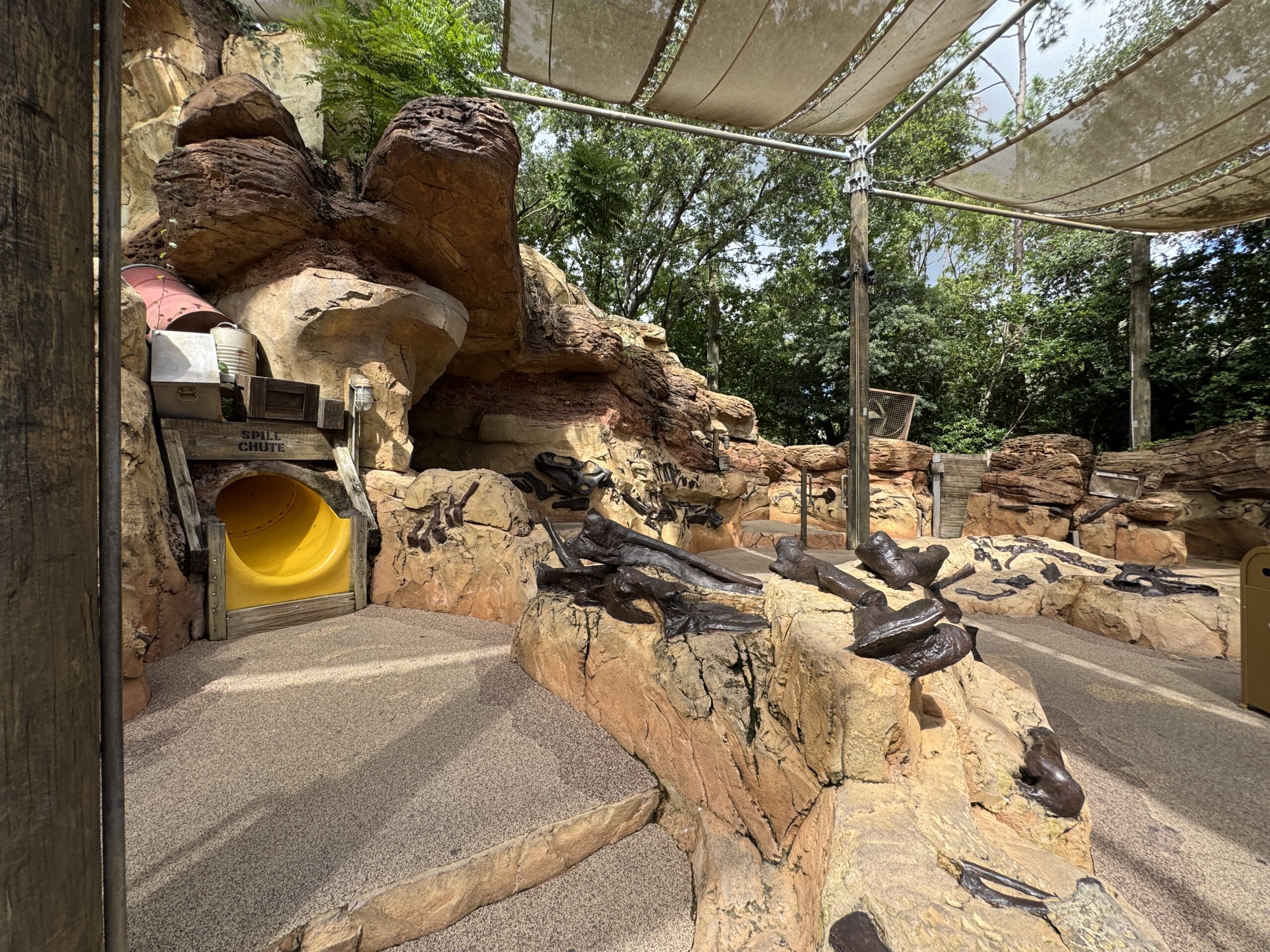 Children’s play area at The Boneyard in Disney's Animal Kingdom, with a yellow tunnel slide, faux rocks, and shaded canopy.