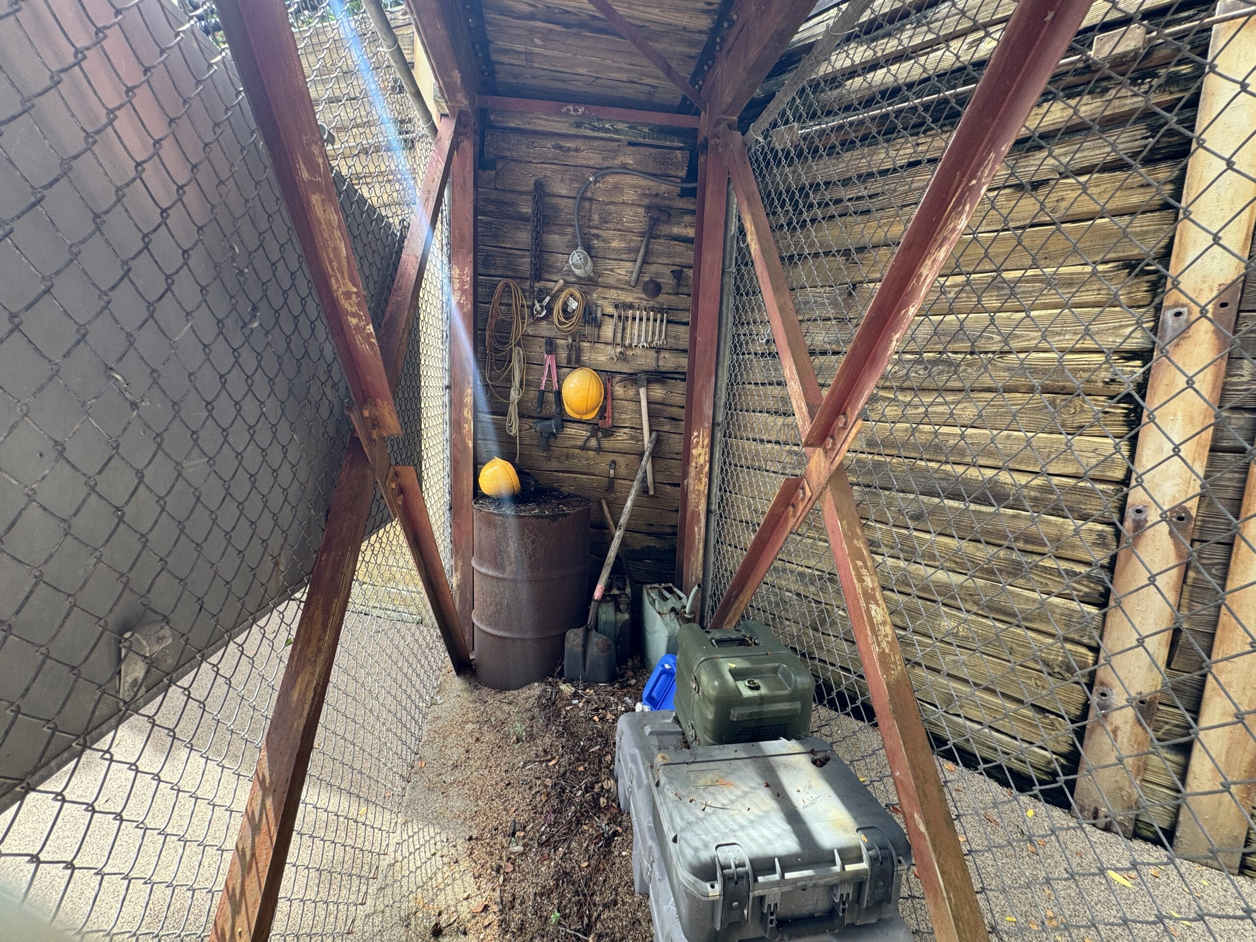 A wooden shelter at The Boneyard in Disney's Animal Kingdom with tools, helmets, and boxes behind chain-link fencing.