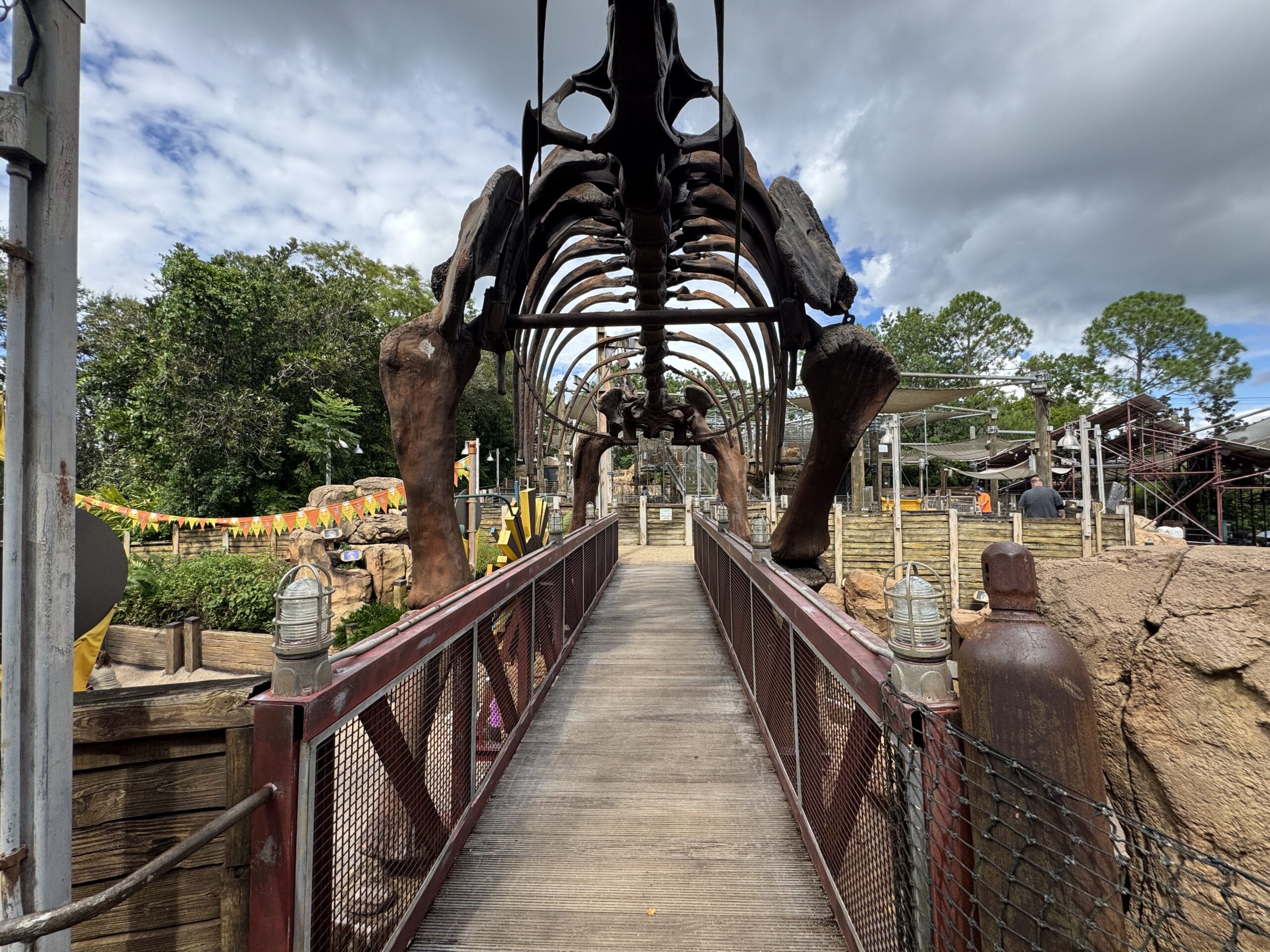 A wooden bridge passes under a large dinosaur skeleton at The Boneyard in Disney's Animal Kingdom park.