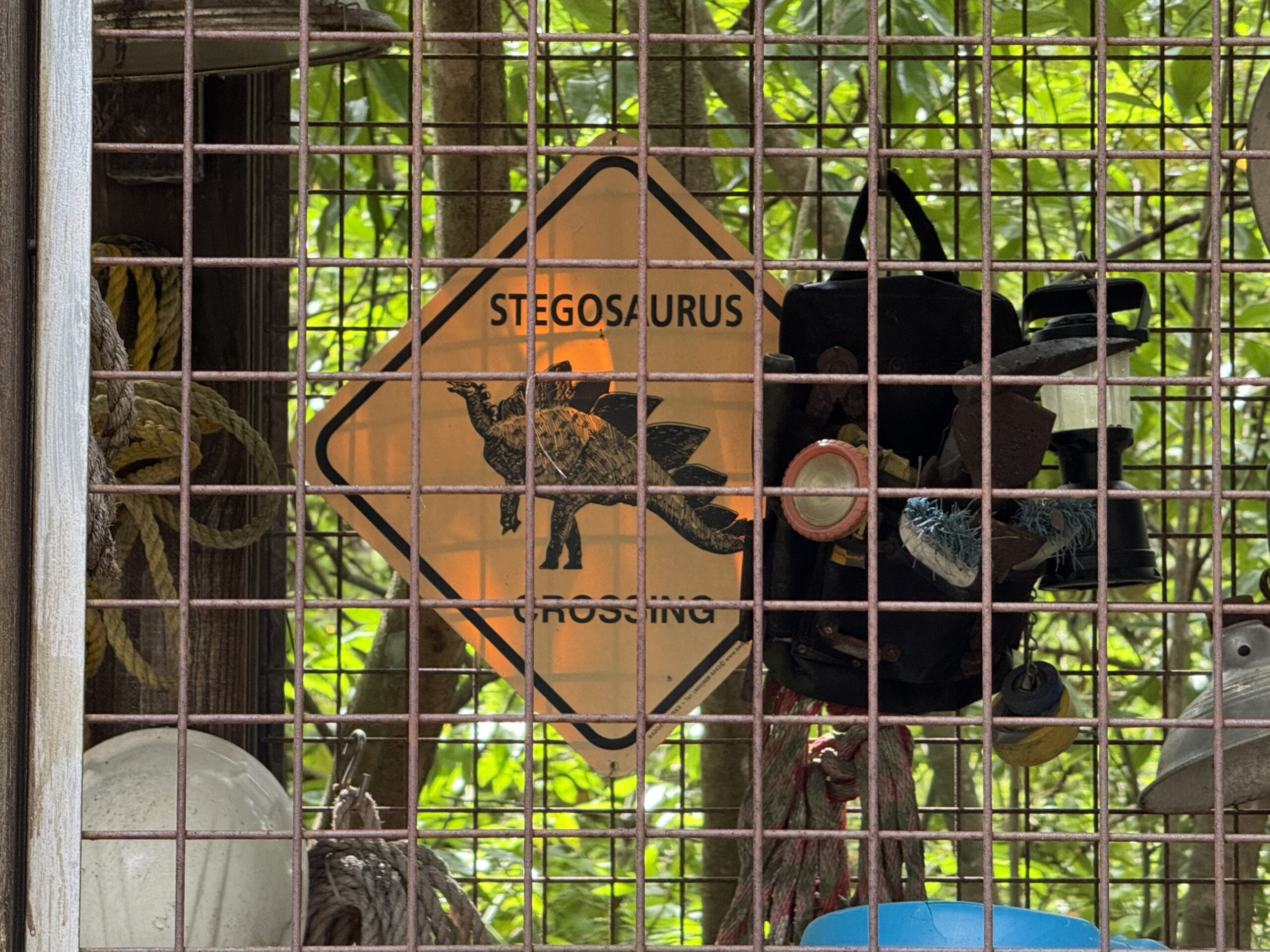 Yellow "Stegosaurus Crossing" sign at The Boneyard in Disney's Animal Kingdom, surrounded by gear and greenery.