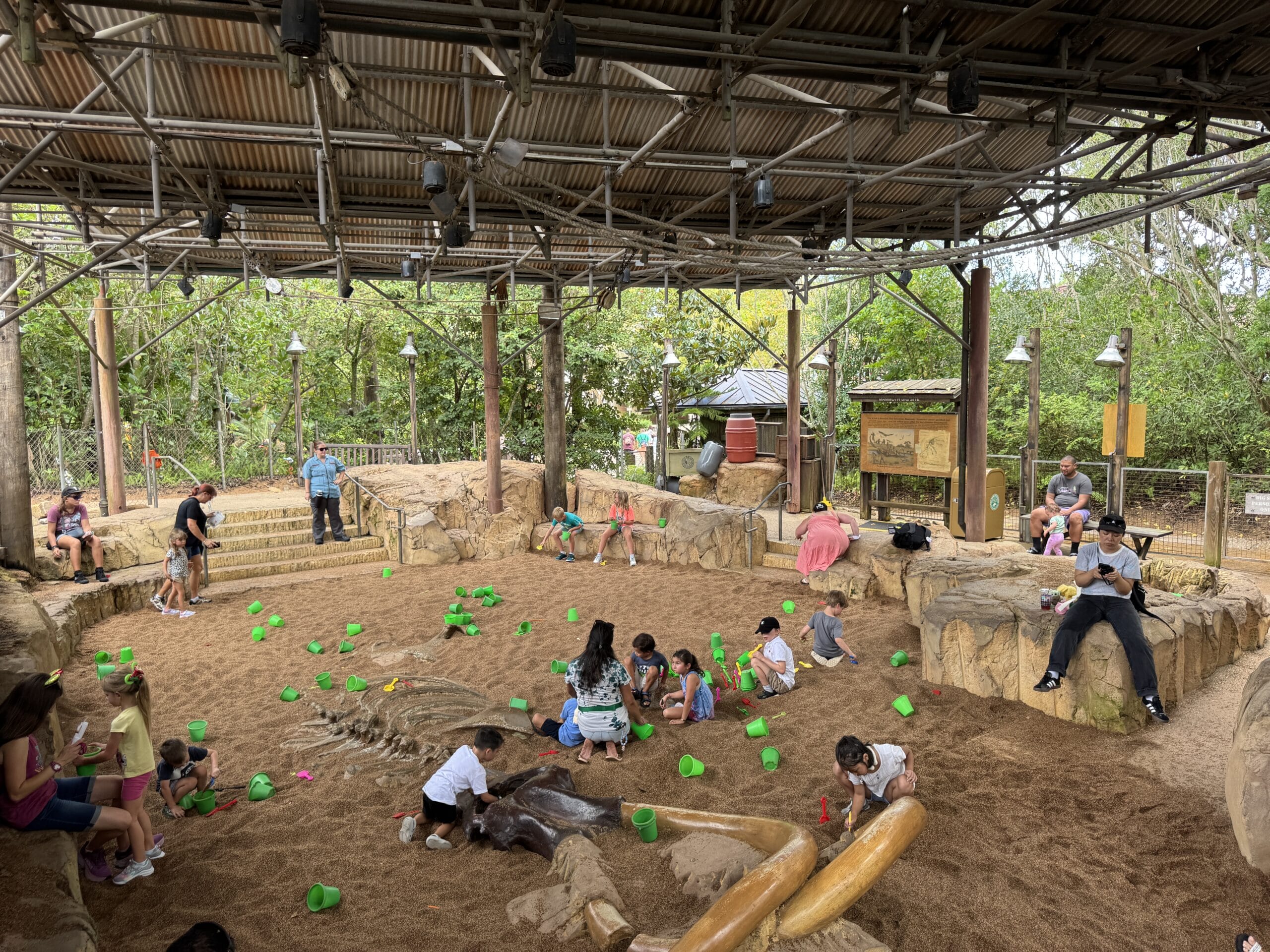 Children dig in a sandy pit with green buckets at The Boneyard, a play area in Disney's Animal Kingdom.