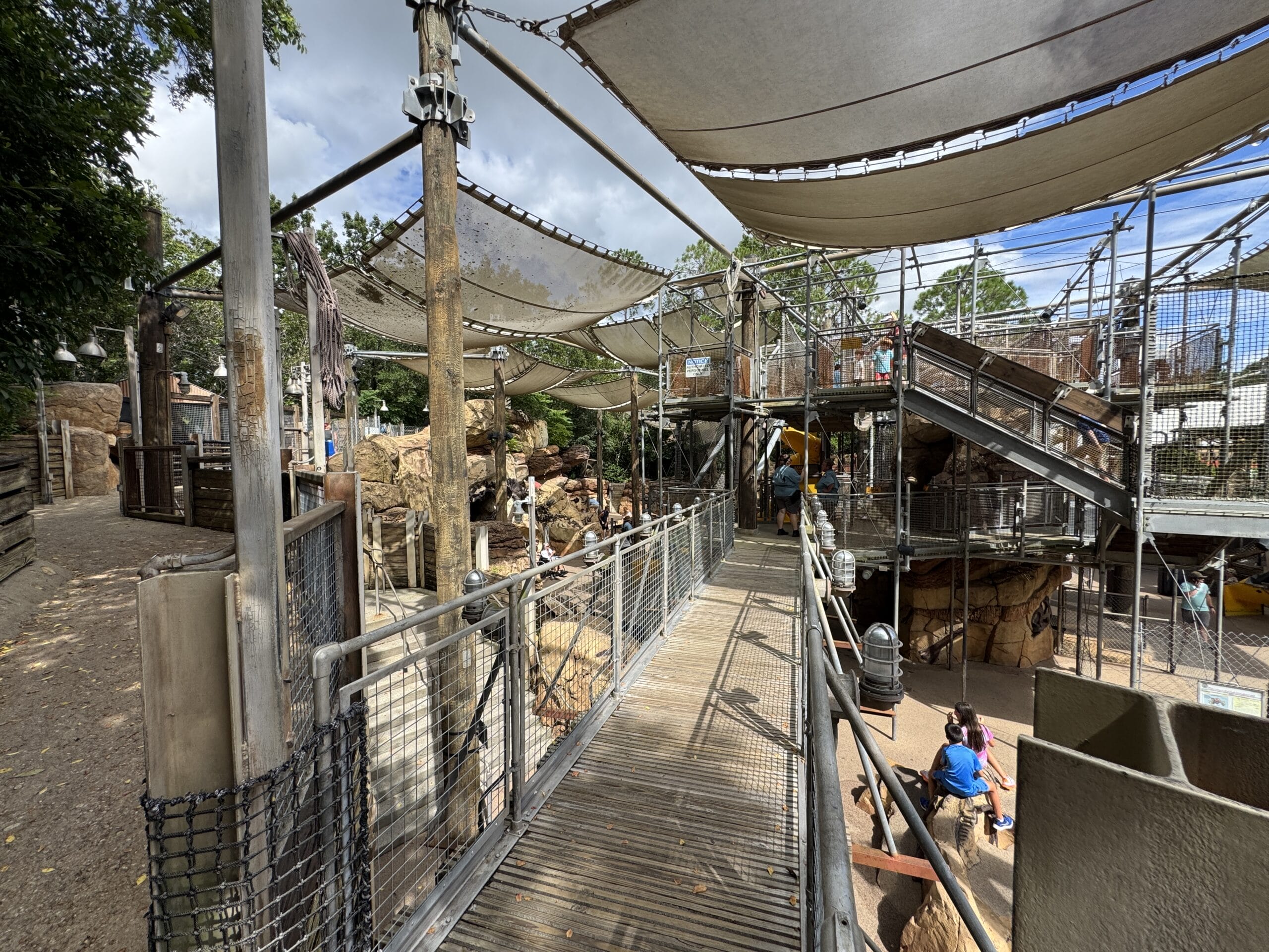 Elevated walkway with shade sails above The Boneyard at Disney's Animal Kingdom; children play and explore below.