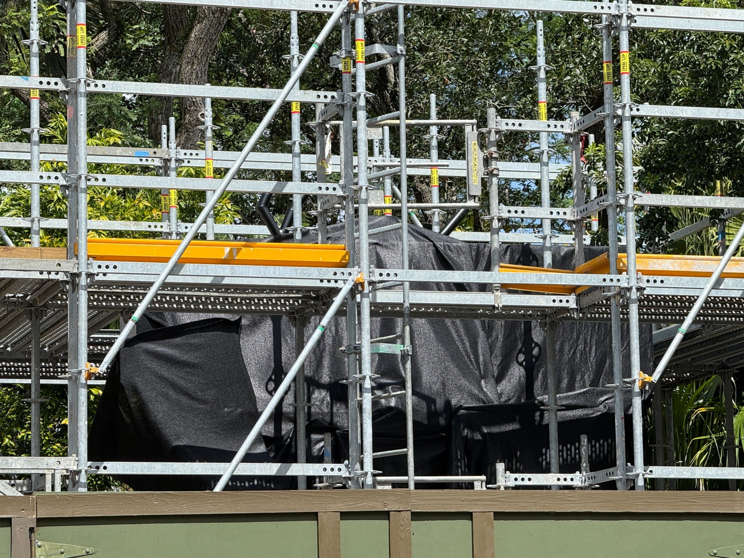 Metal scaffolding with black tarp, trees, and a Better Zoogether Sign at Disney's Animal Kingdom on a sunny day.