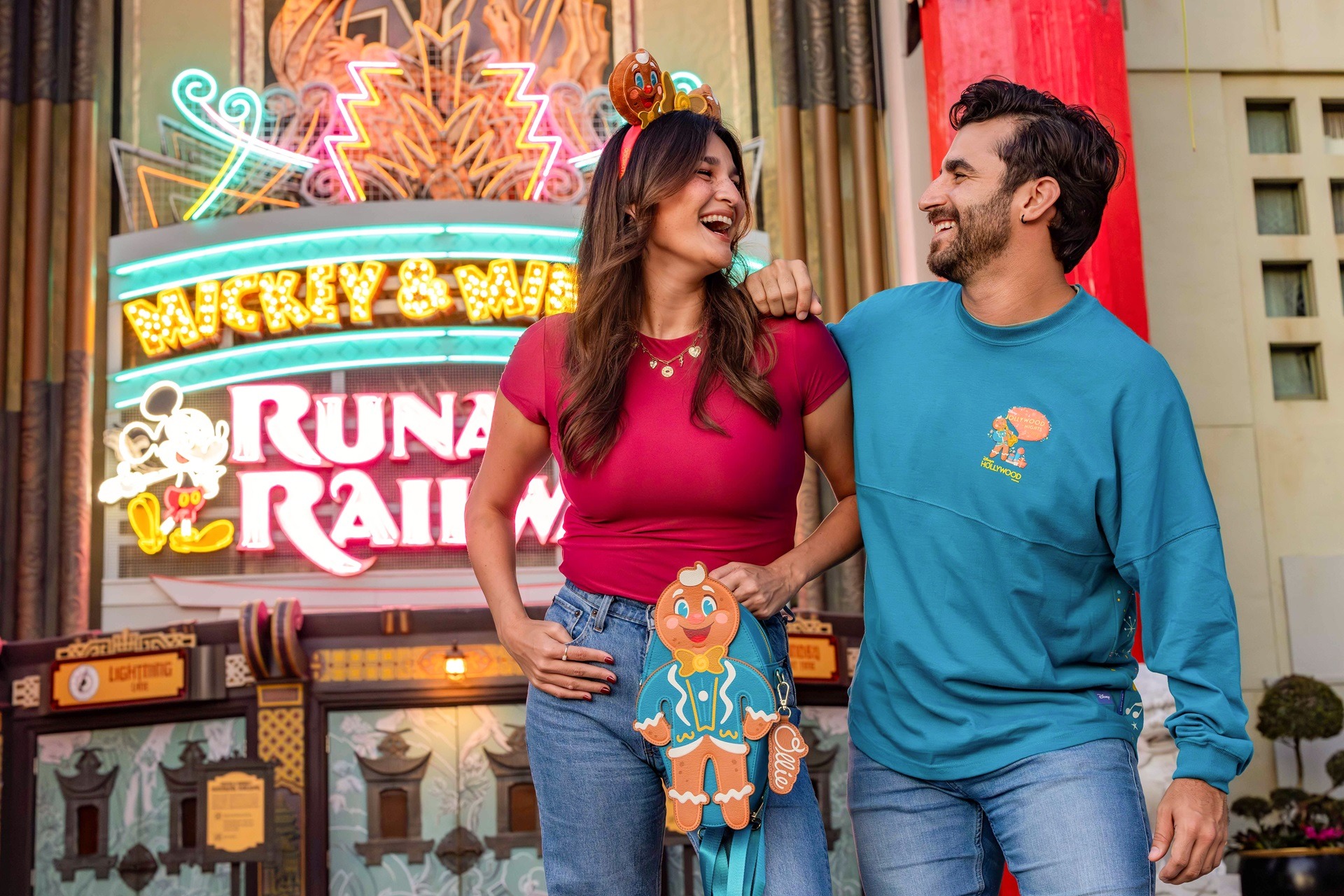 A smiling couple outside Mickey & Minnie's Runaway Railway holds an Ollie the Gingerbread Man souvenir.
