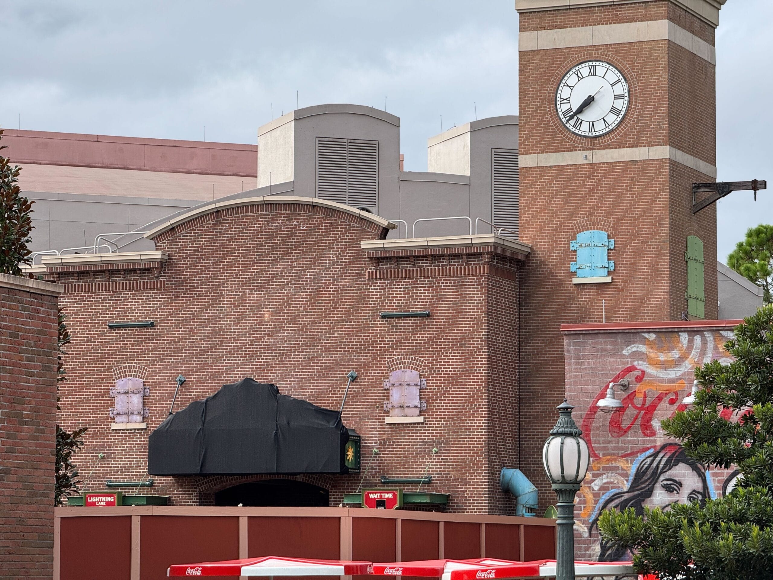 A brick building with a Clock Tower and Coca-Cola mural, reminiscent of MuppetVision, stands under a cloudy sky.