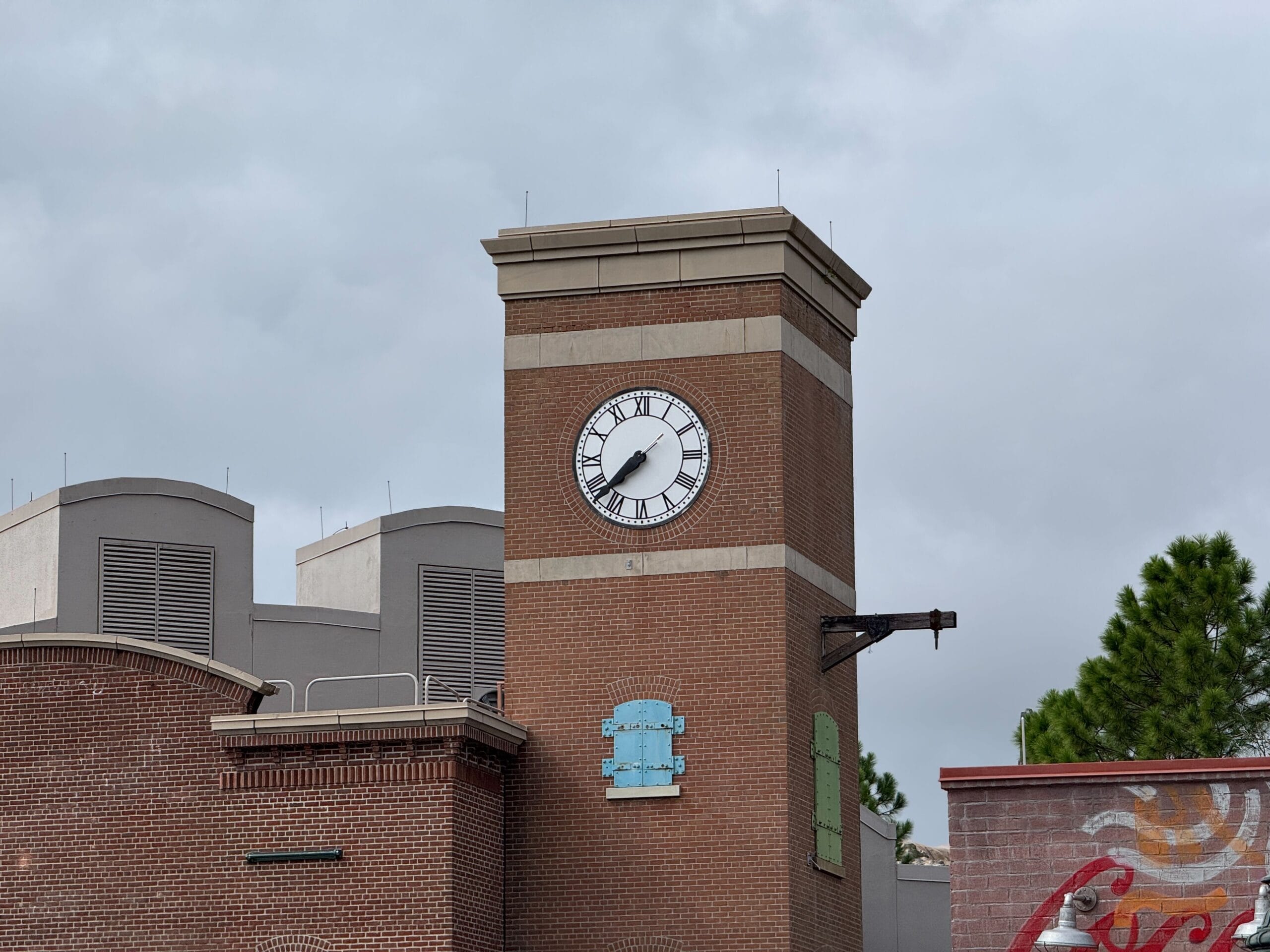 A brick Clock Tower shows 11:56 against a cloudy sky, with trees and buildings in the background, evoking MuppetVision charm.