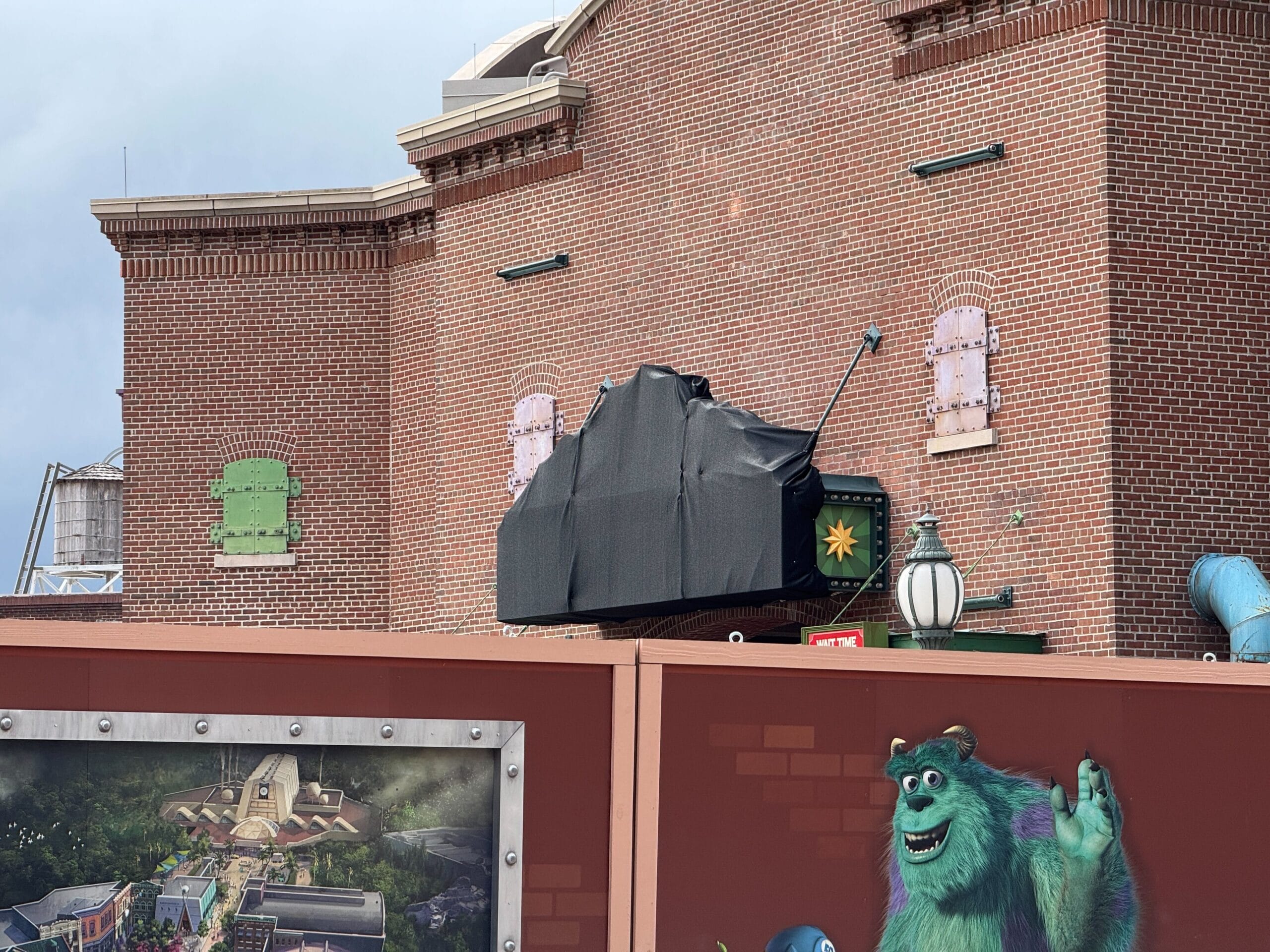 A brick building with a covered sign, construction wall, and Gonzo cartoon monster on the front wall.