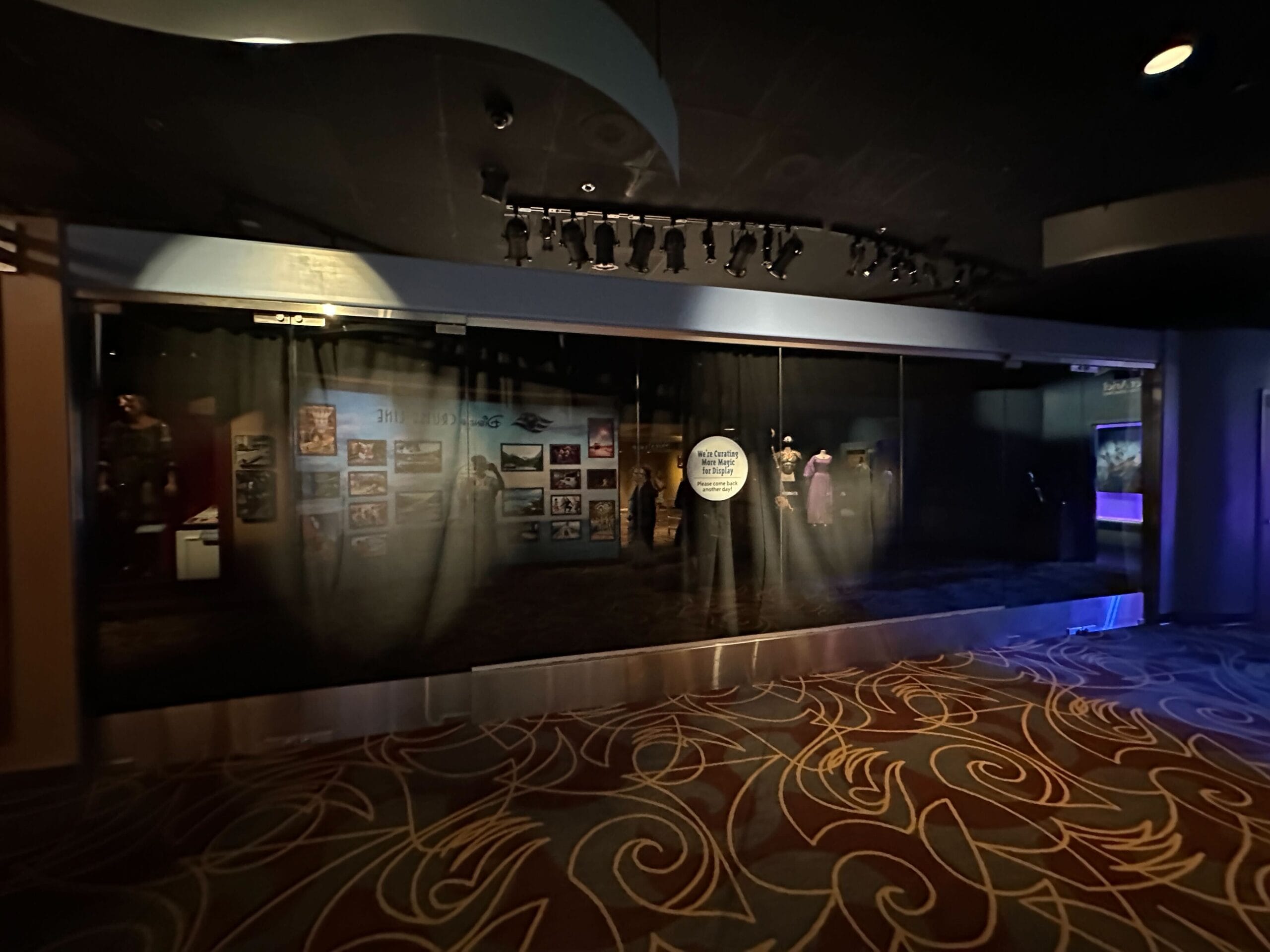 Dimly lit One Man's Dream exhibit behind glass, with photos, mannequins in costume, and patterned carpet at Disney's Hollywood Studios.