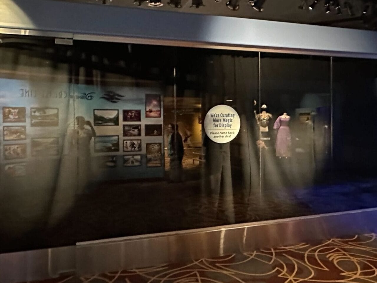 A dimly lit museum exhibit at One Man's Dream features photos and displays behind glass, patterned carpet in the foreground.