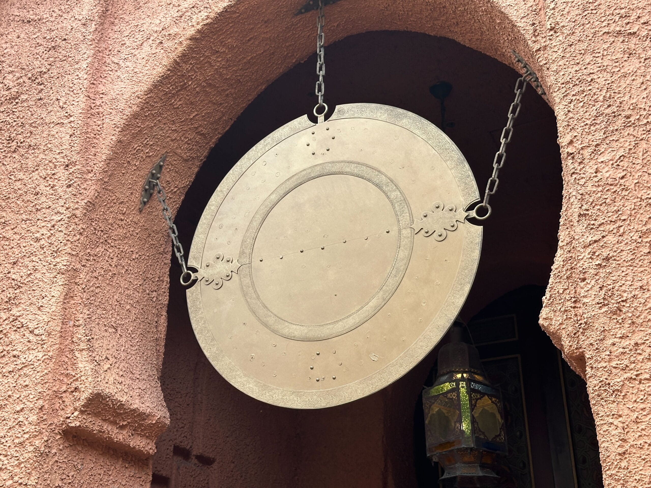 Large round metal sign hanging by chains above an arched doorway with textured, reddish walls.