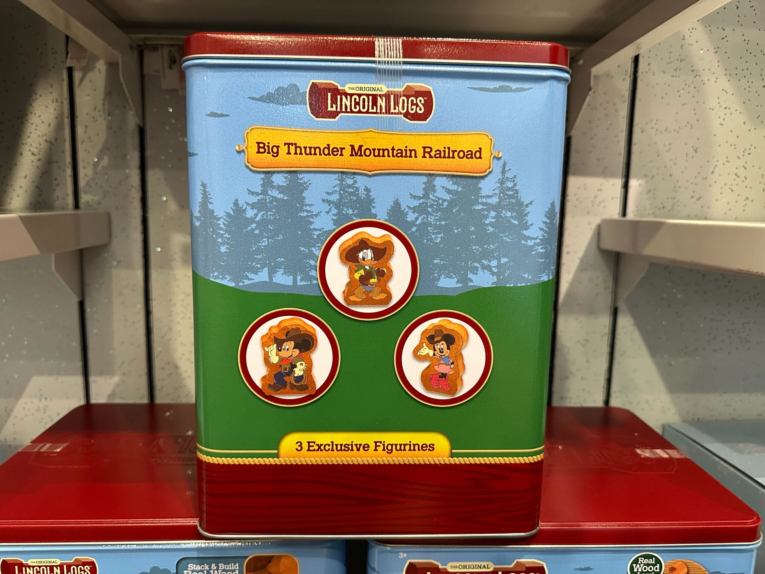 A Lincoln Logs Big Thunder Mountain Railroad tin featuring 3 exclusive figurines on a shelf.
