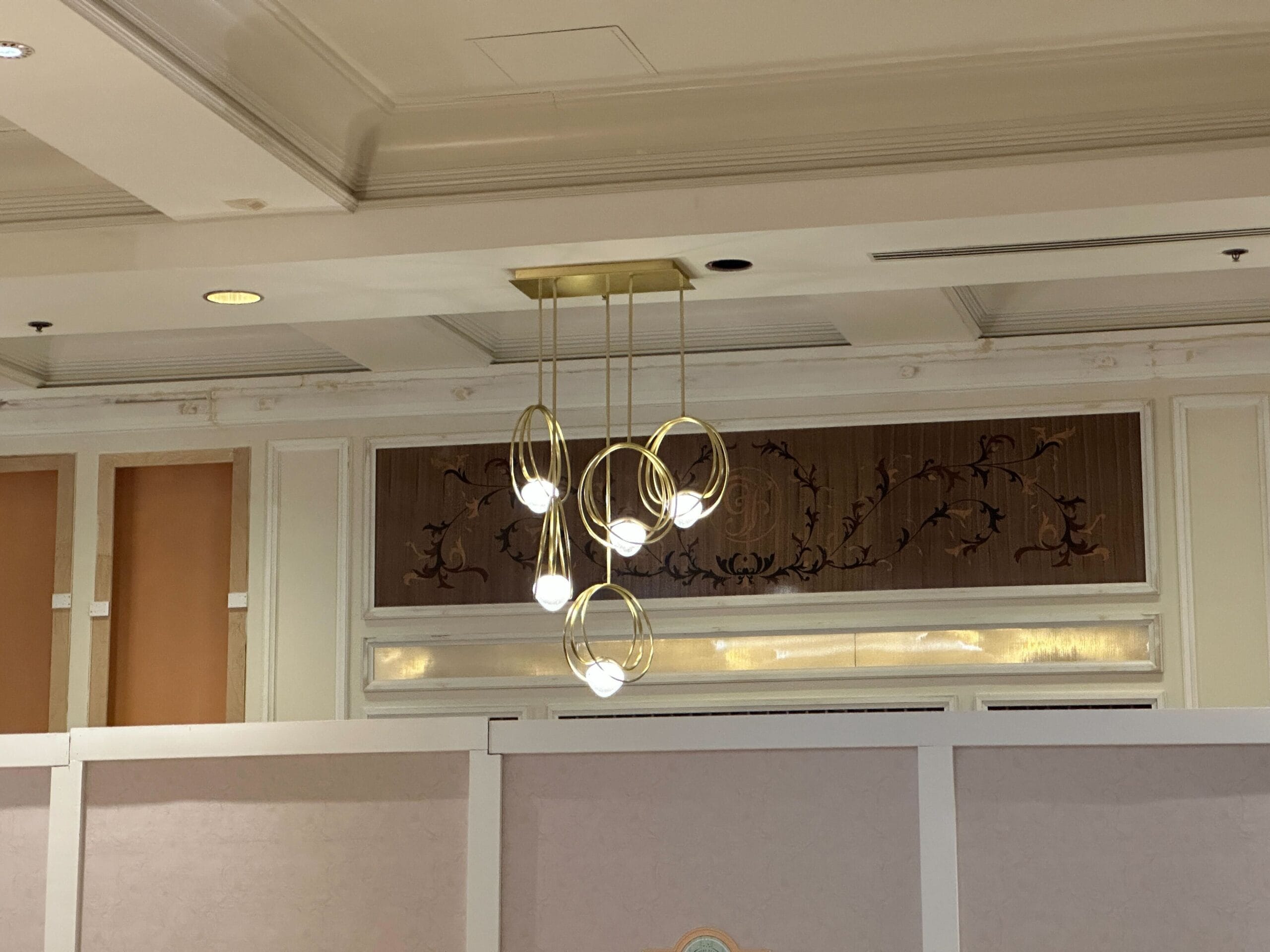 Modern chandelier with spherical lights and gold rings hanging from a ceiling in an elegant room with decorative wall accents.