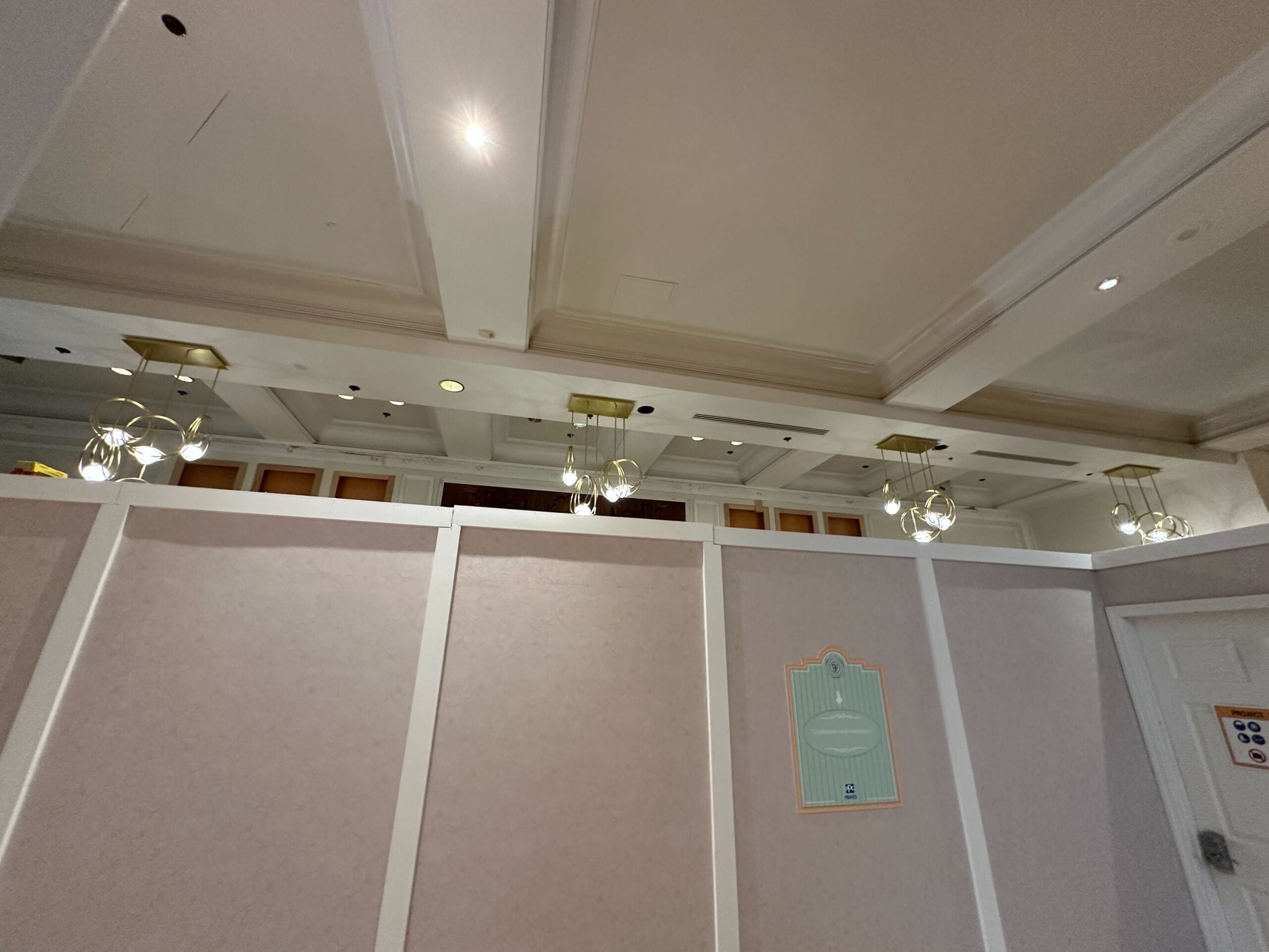 A construction wall with a sign blocks off a hallway; ceiling lights and vents are visible above the wall.