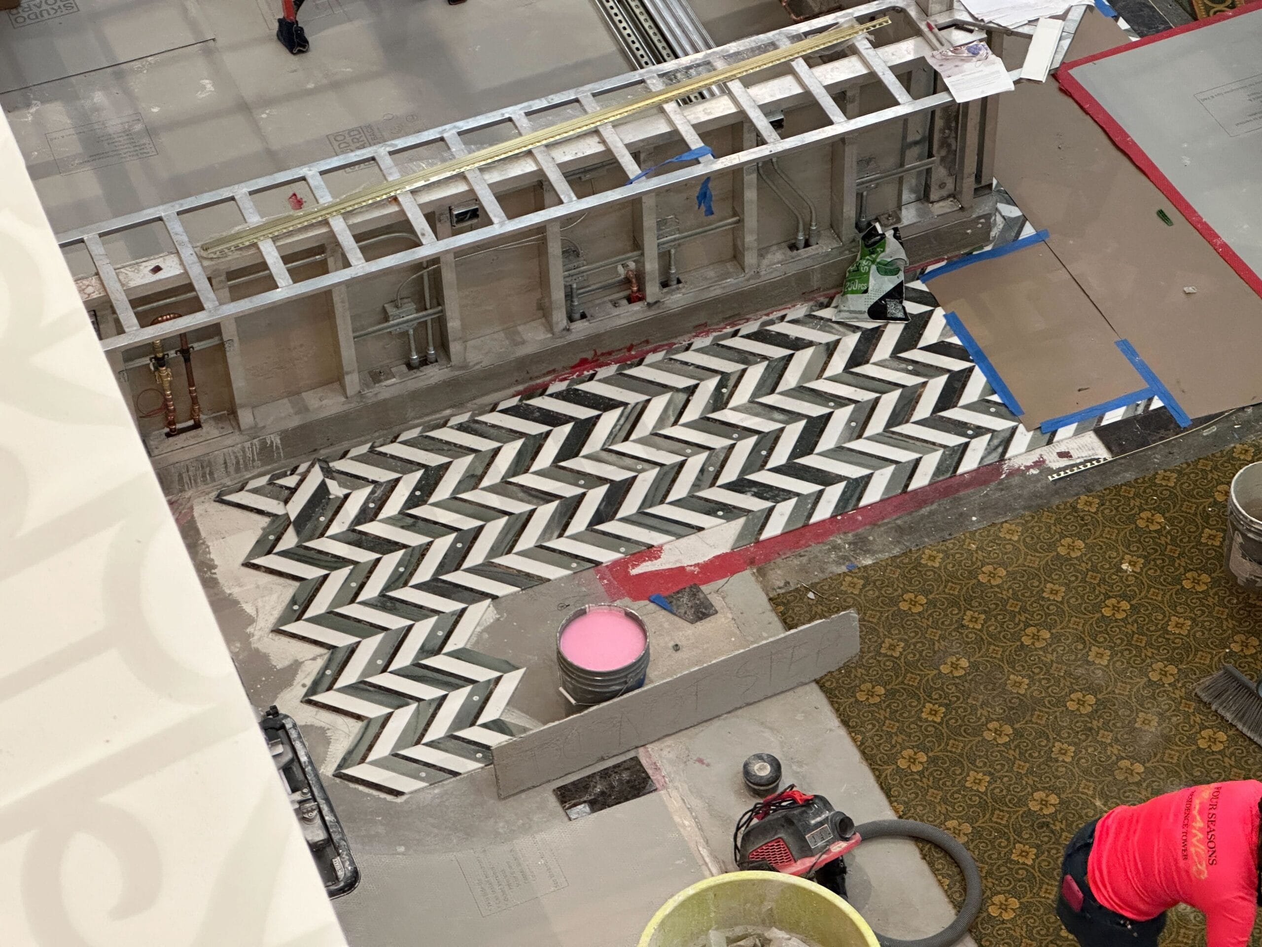 A black and white chevron tile pattern being installed on a floor at a construction site, viewed from above.