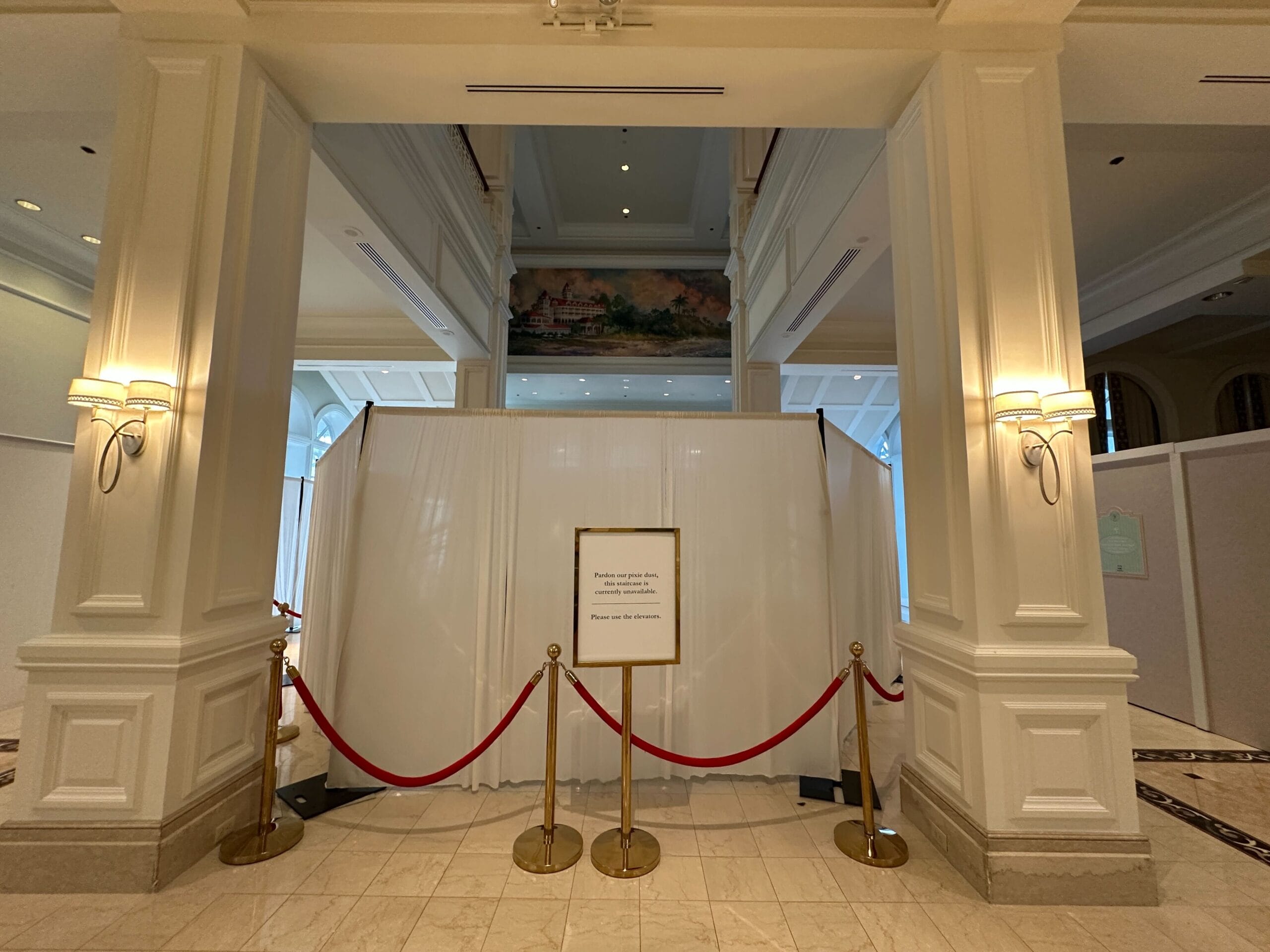 A section of a hotel lobby is closed off with white curtains, red ropes, and a sign in front.