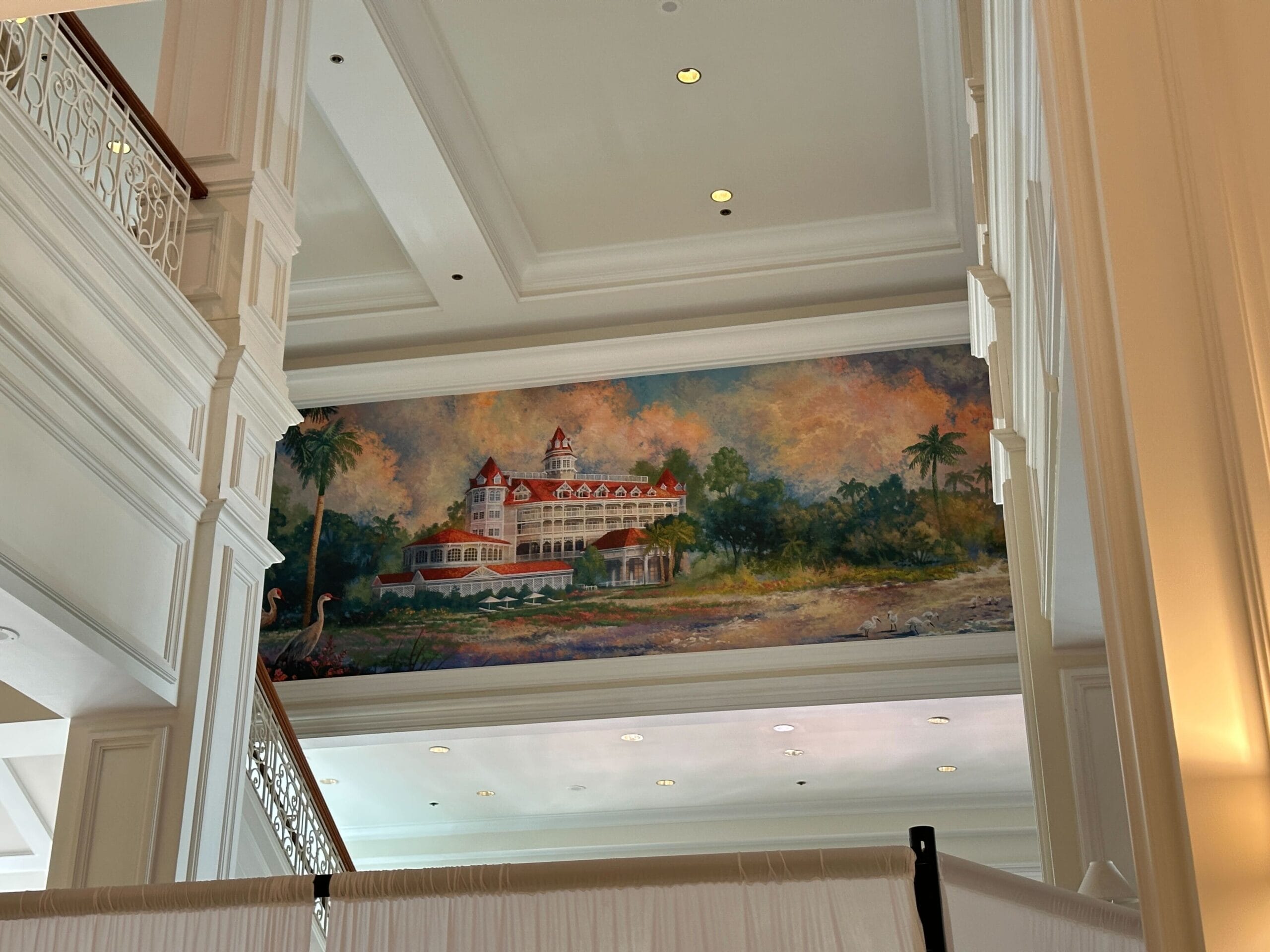 Wall mural of the Grand Floridian Resort amid trees, seen above white railings and tile flooring indoors.