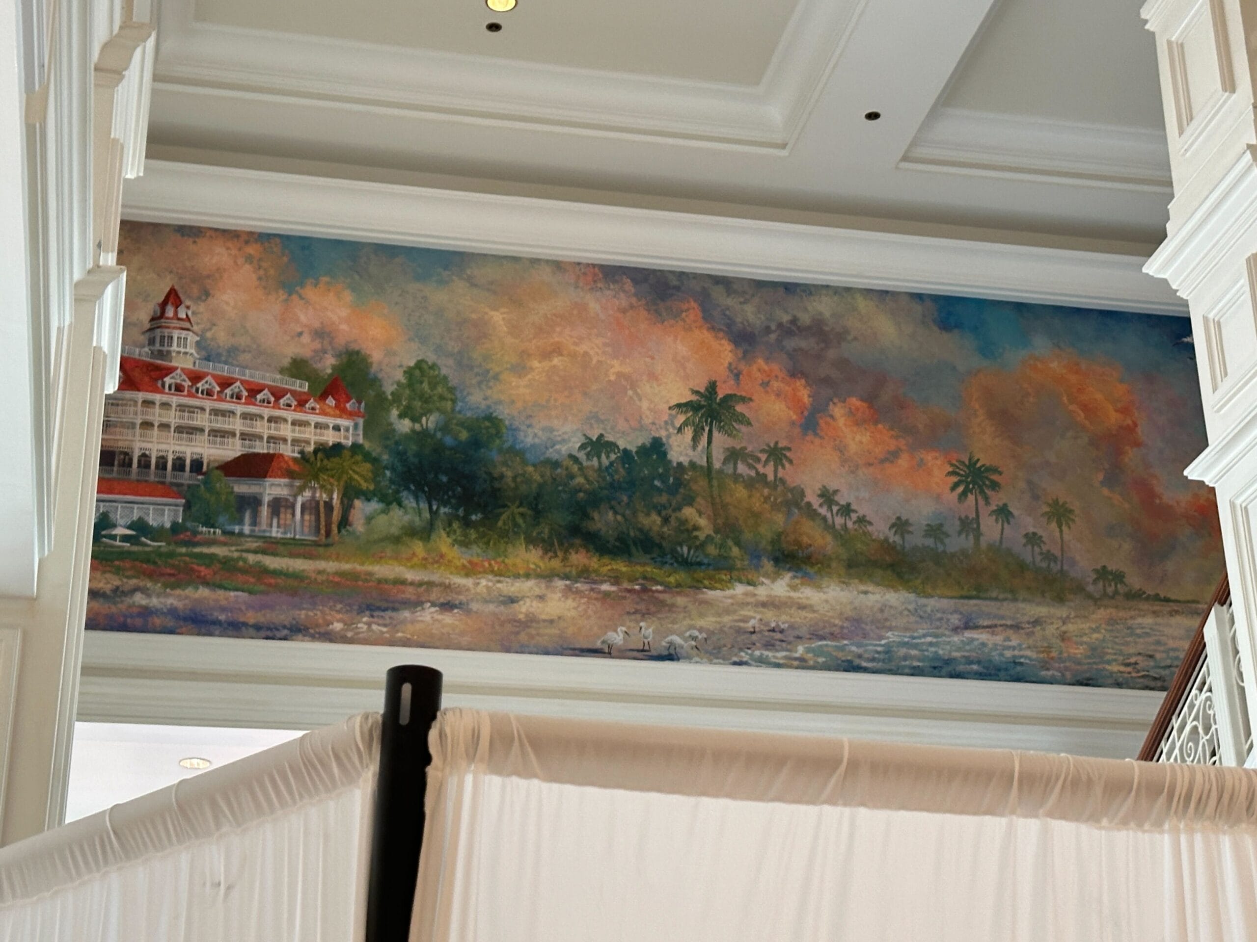 A mural of Disney's Grand Floridian Resort with palm trees and vivid sky, partly hidden by a white barrier in the foreground.