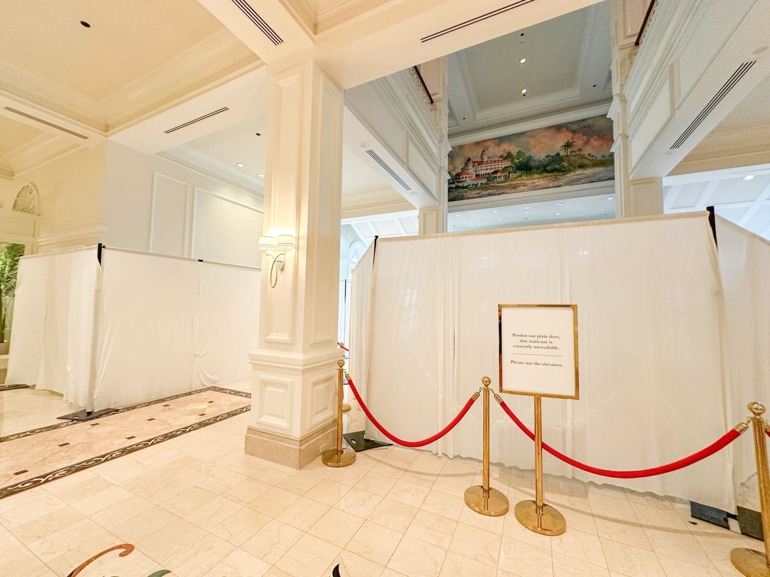 White curtains section off part of a hotel lobby, with a sign and red ropes blocking access to the area.