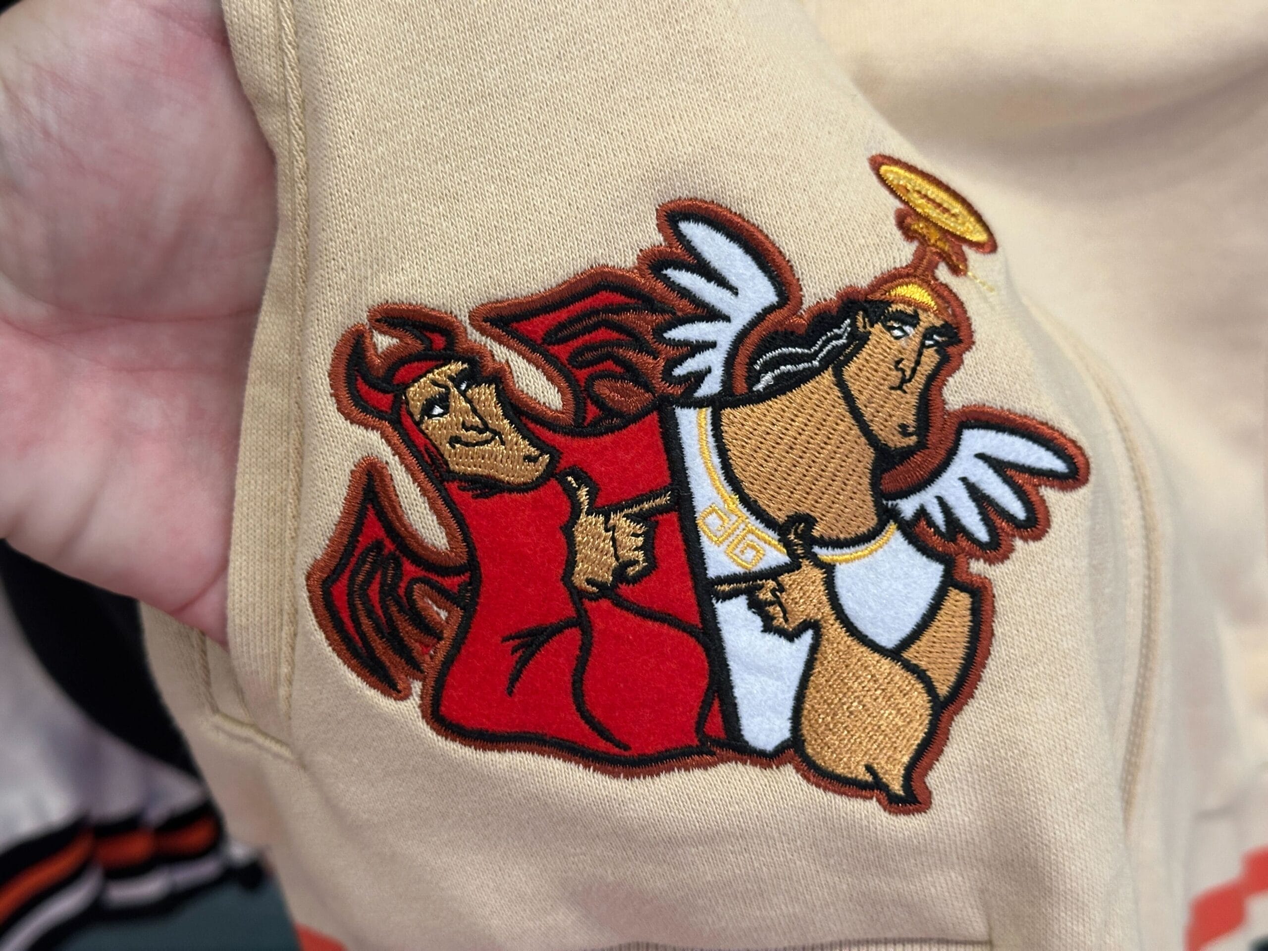 Cartoon devil and angel Kronk, like Disney Letterman Jackets, sewn onto tan fabric.